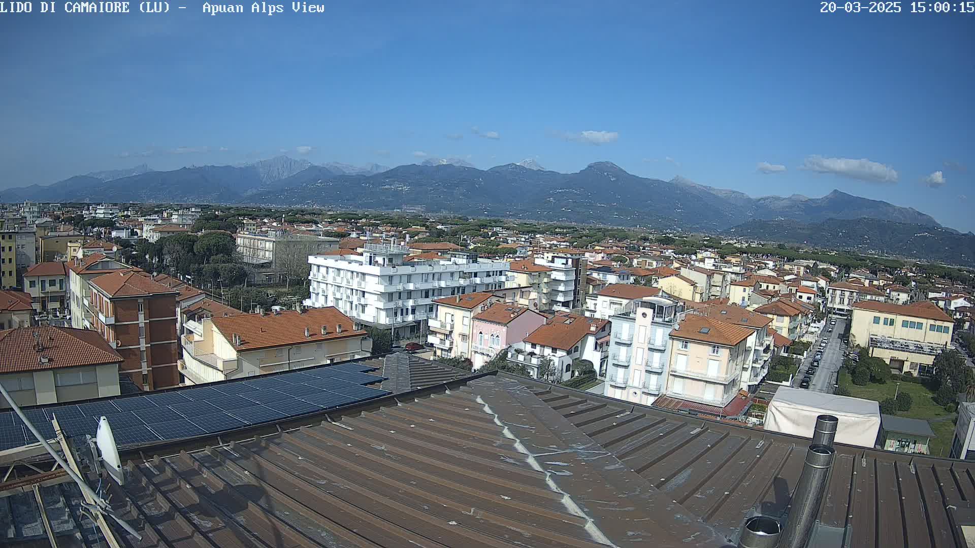 A rooftop view of a town nestled against a backdrop of mountains under a clear blue sky.