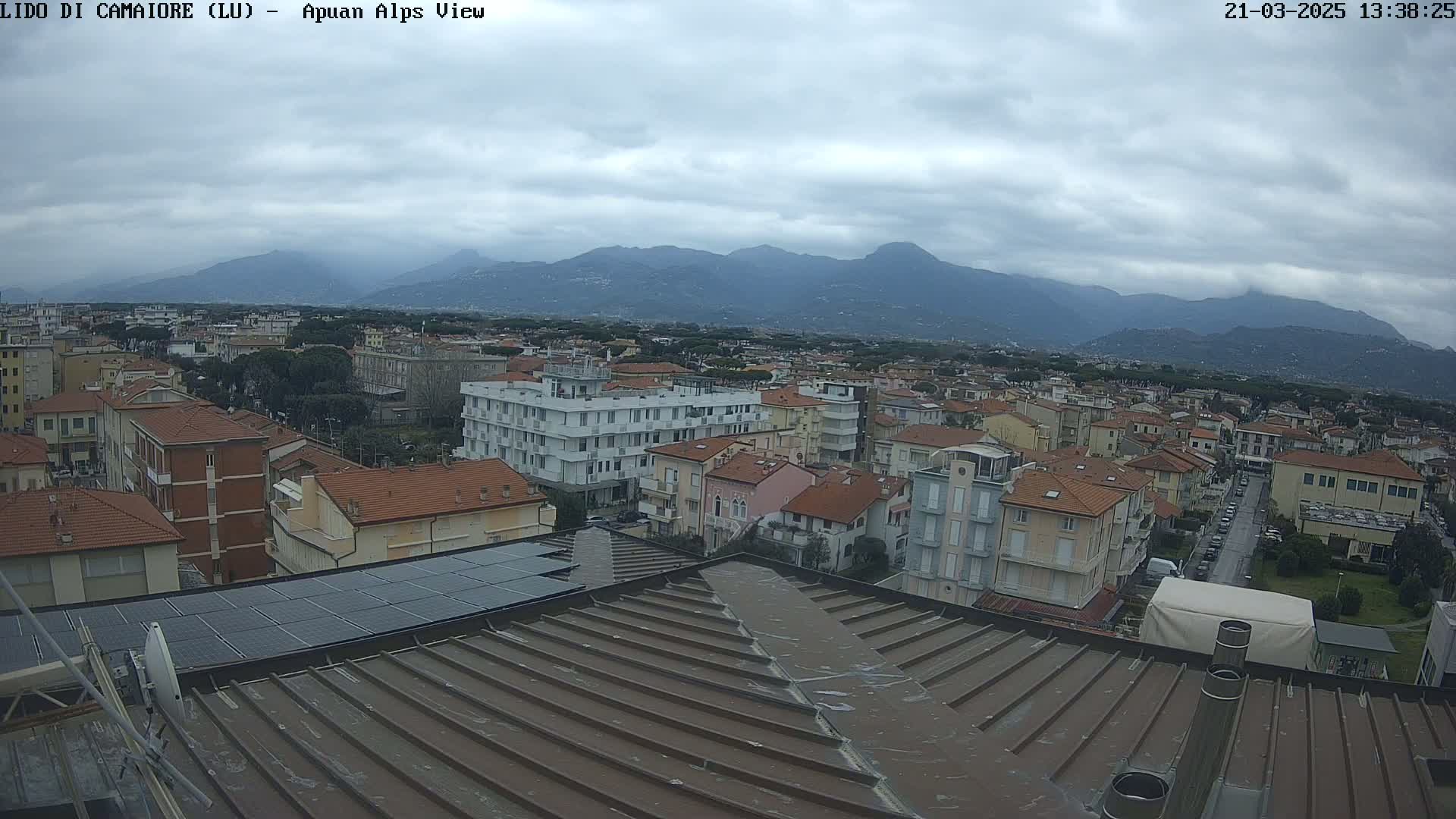 A view of a town under a cloudy sky, with mountains visible in the distance.