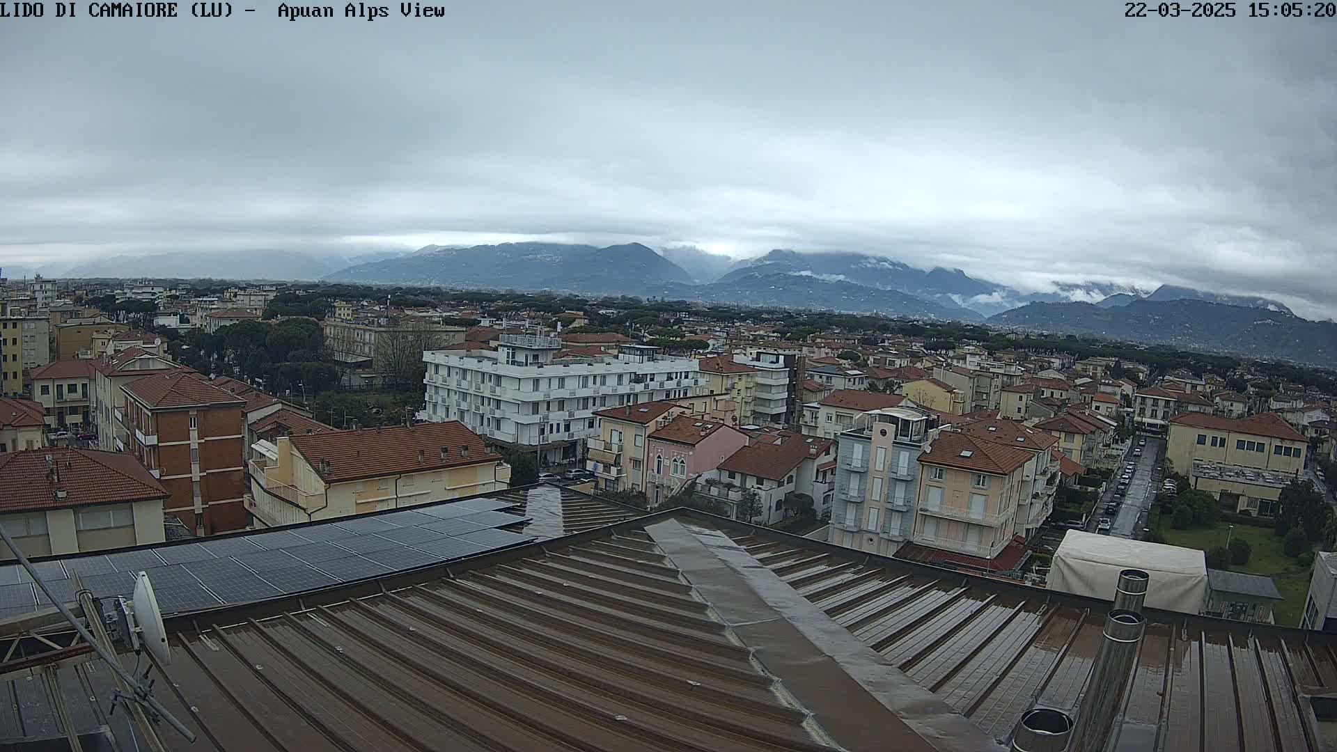 A wet rooftop overlooks a town nestled against a mountain range under a cloudy sky.