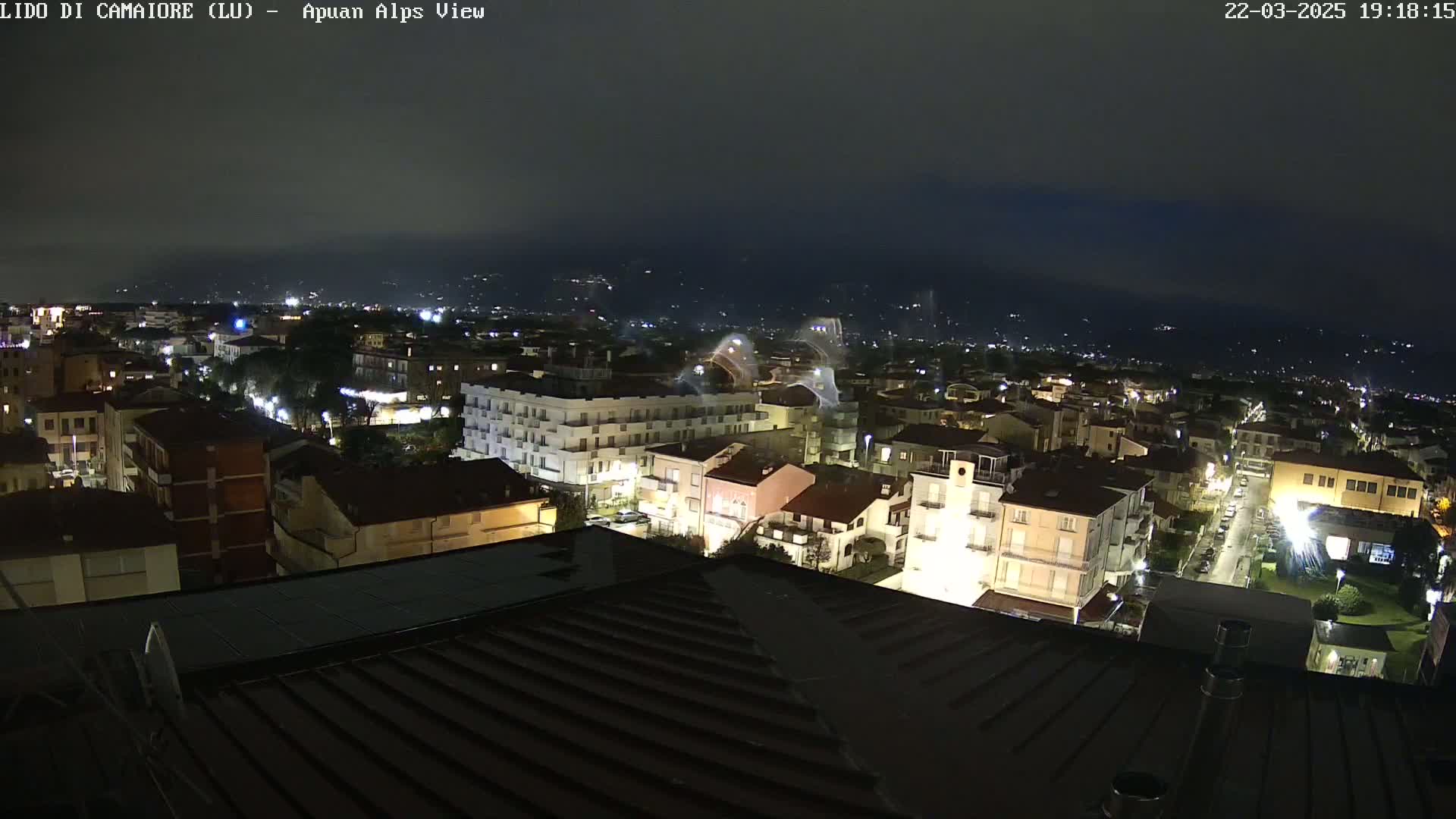 A nighttime view of a town illuminated by streetlights, with dimly lit mountains in the background under a dark sky.