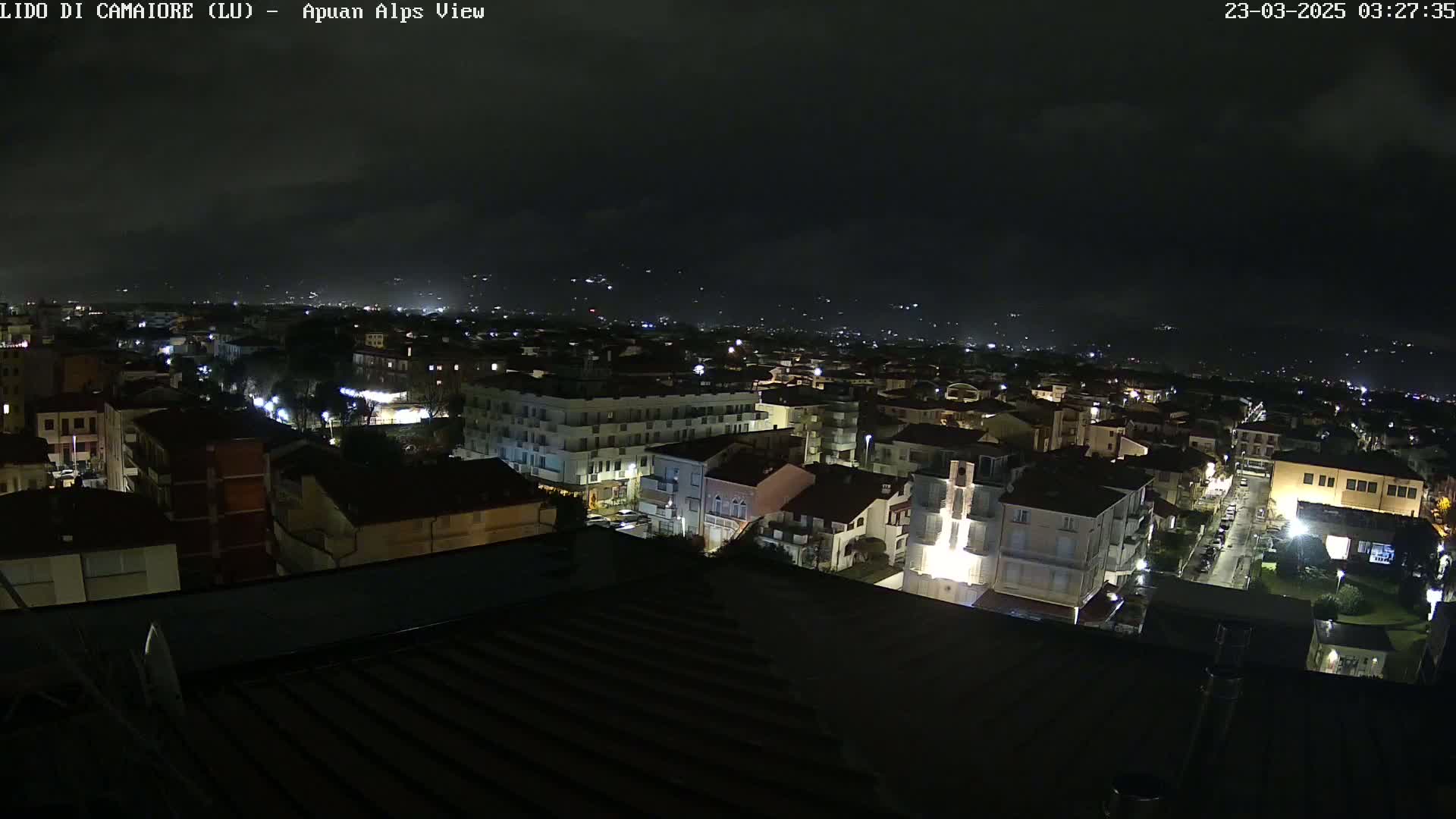 A nighttime view of a city under a cloudy sky, showing many buildings illuminated by streetlights.