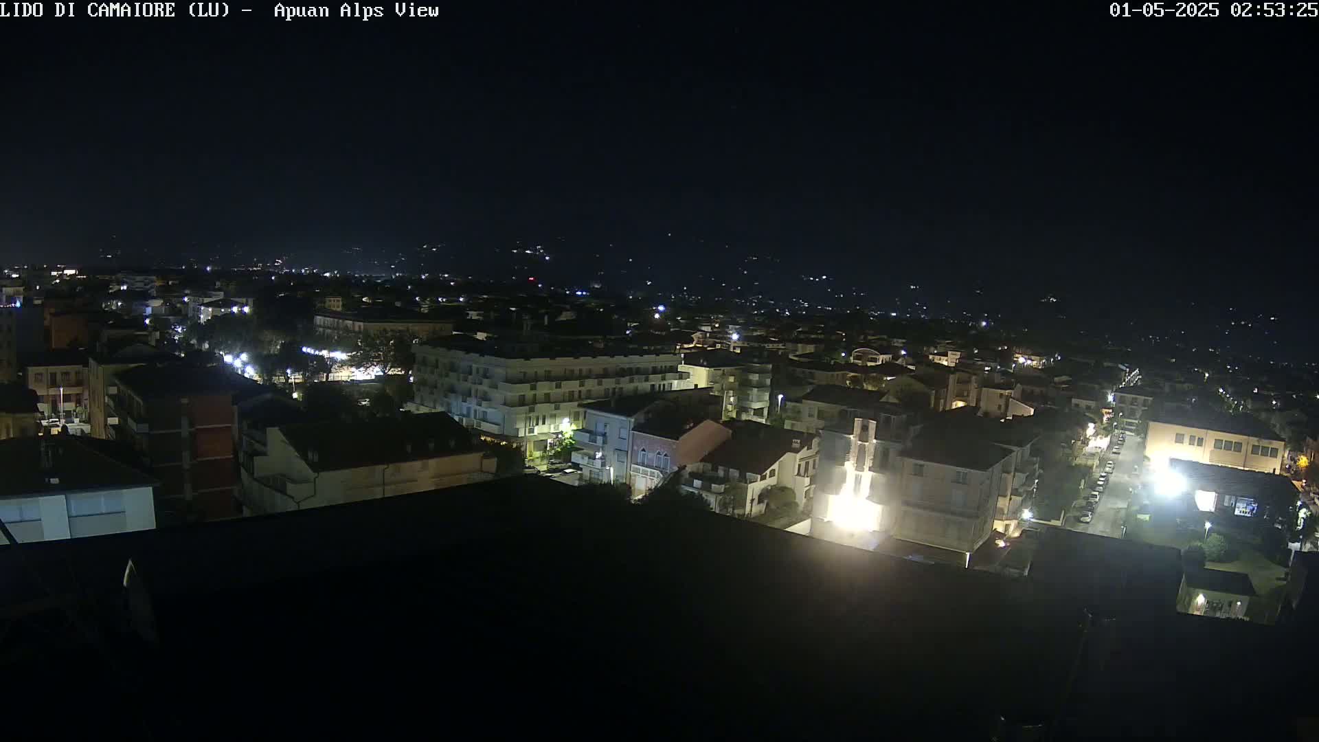 A nighttime, high-angle view of a town with illuminated buildings and streets, under a dark sky.