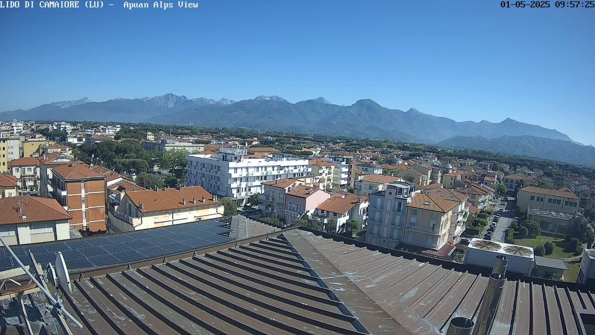 A clear, sunny day reveals a rooftop view of a town nestled below a mountain range.