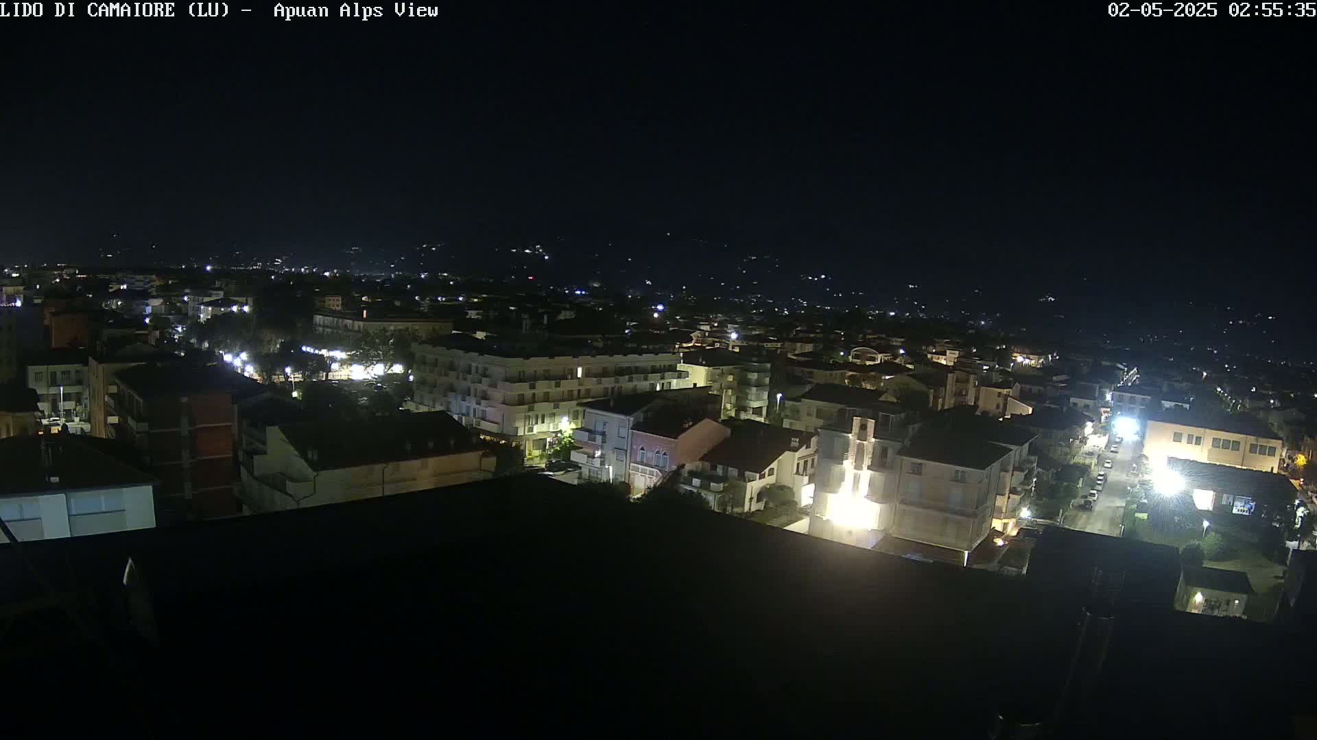 A nighttime, aerial view of a town illuminated by streetlights and building lights, with dark, clear skies.