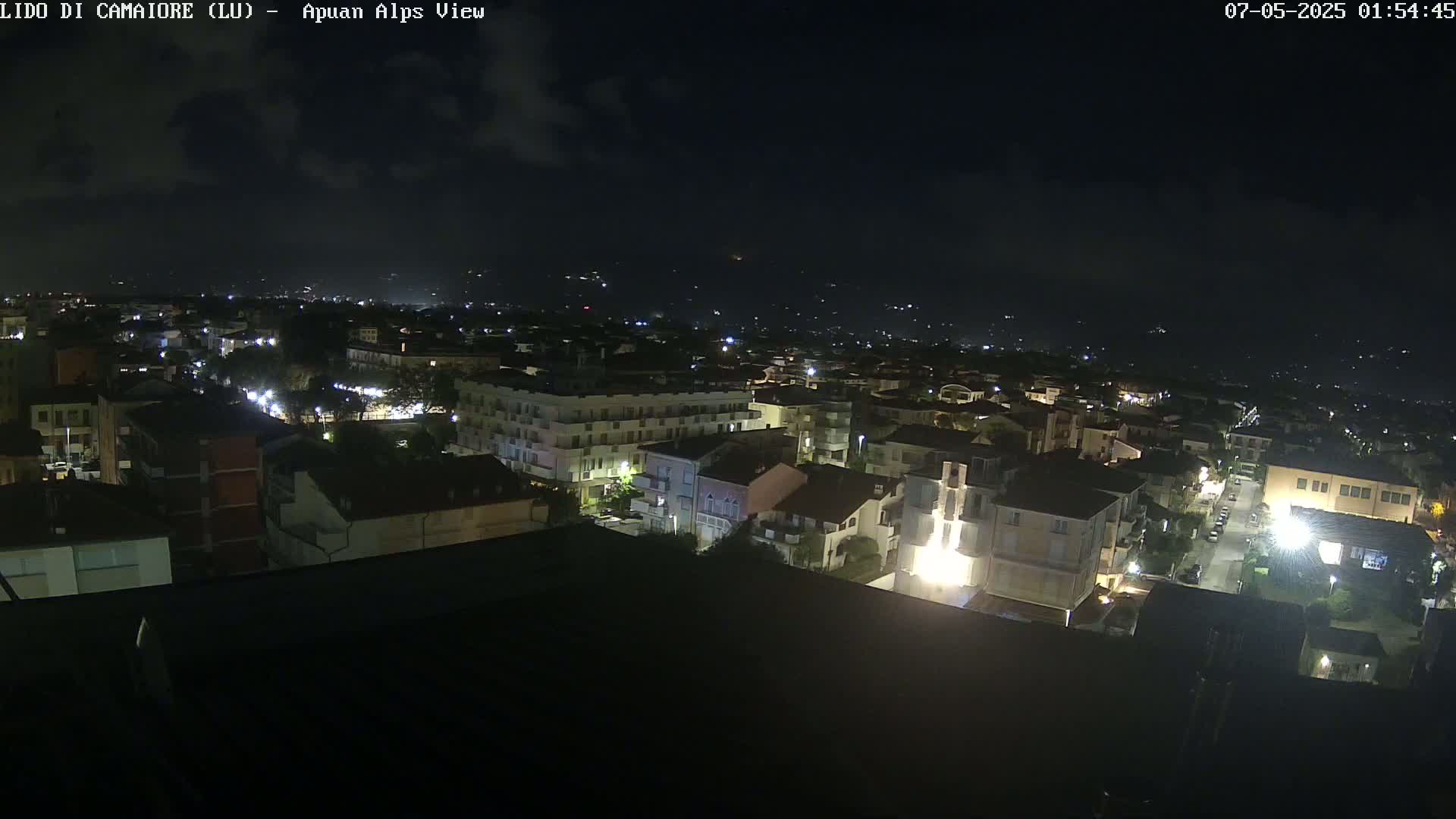 A nighttime aerial view of a town illuminated by streetlights under a partly cloudy sky.