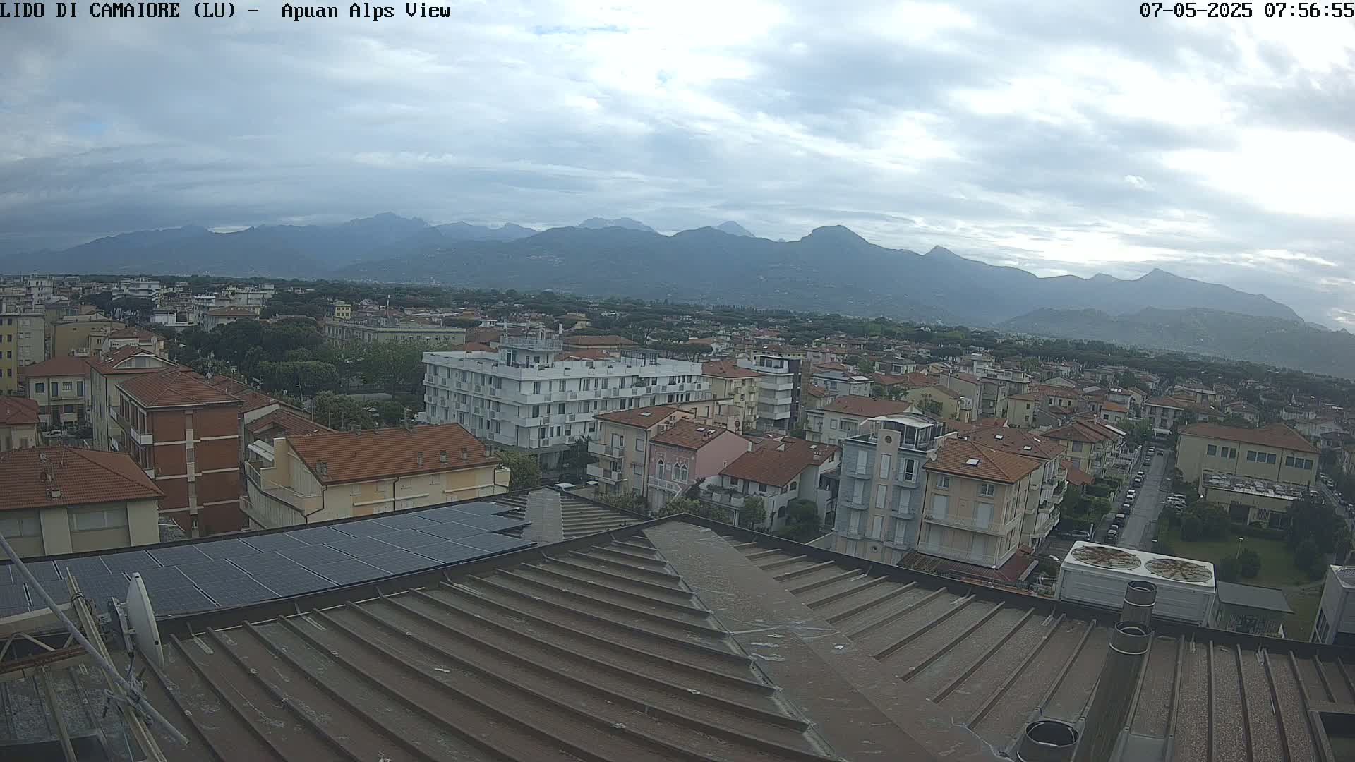 A rooftop view of a town nestled in a valley, with mountains in the background under a cloudy sky.