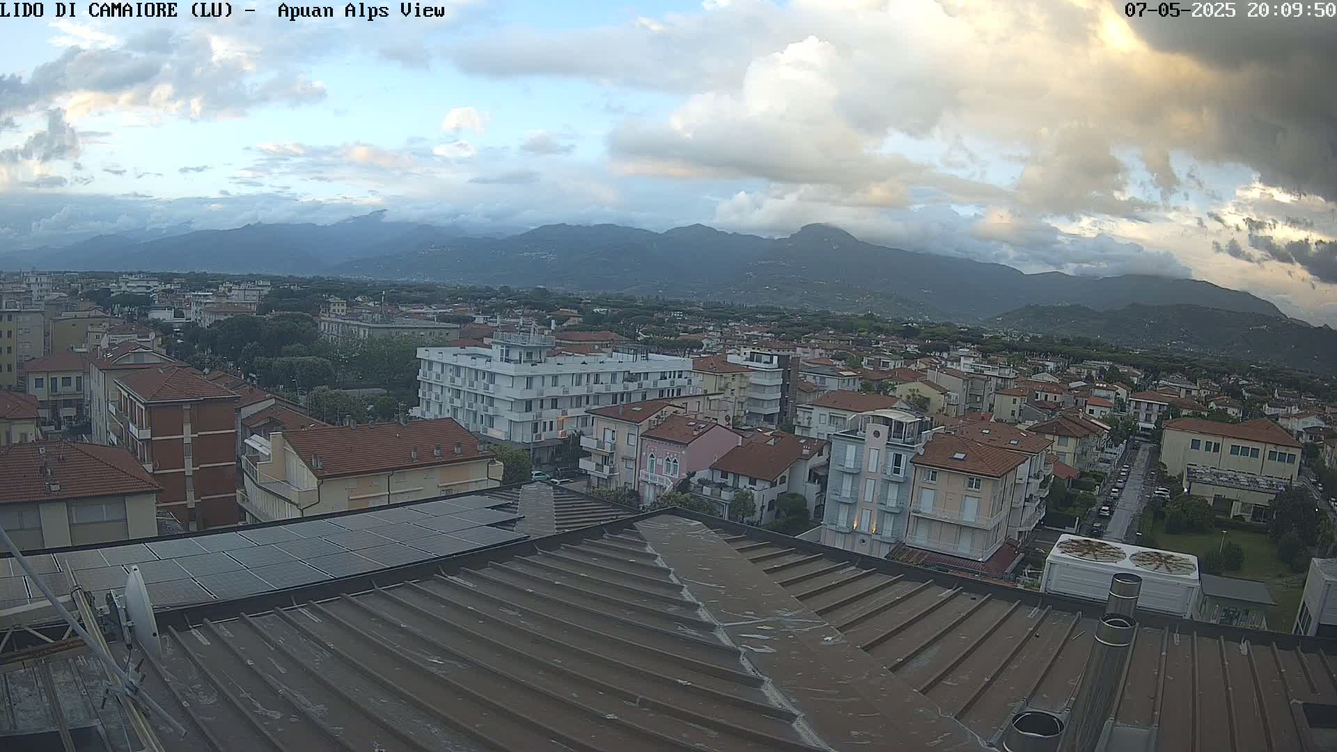 A cloudy evening view of a town nestled in a valley, with mountains in the distance.