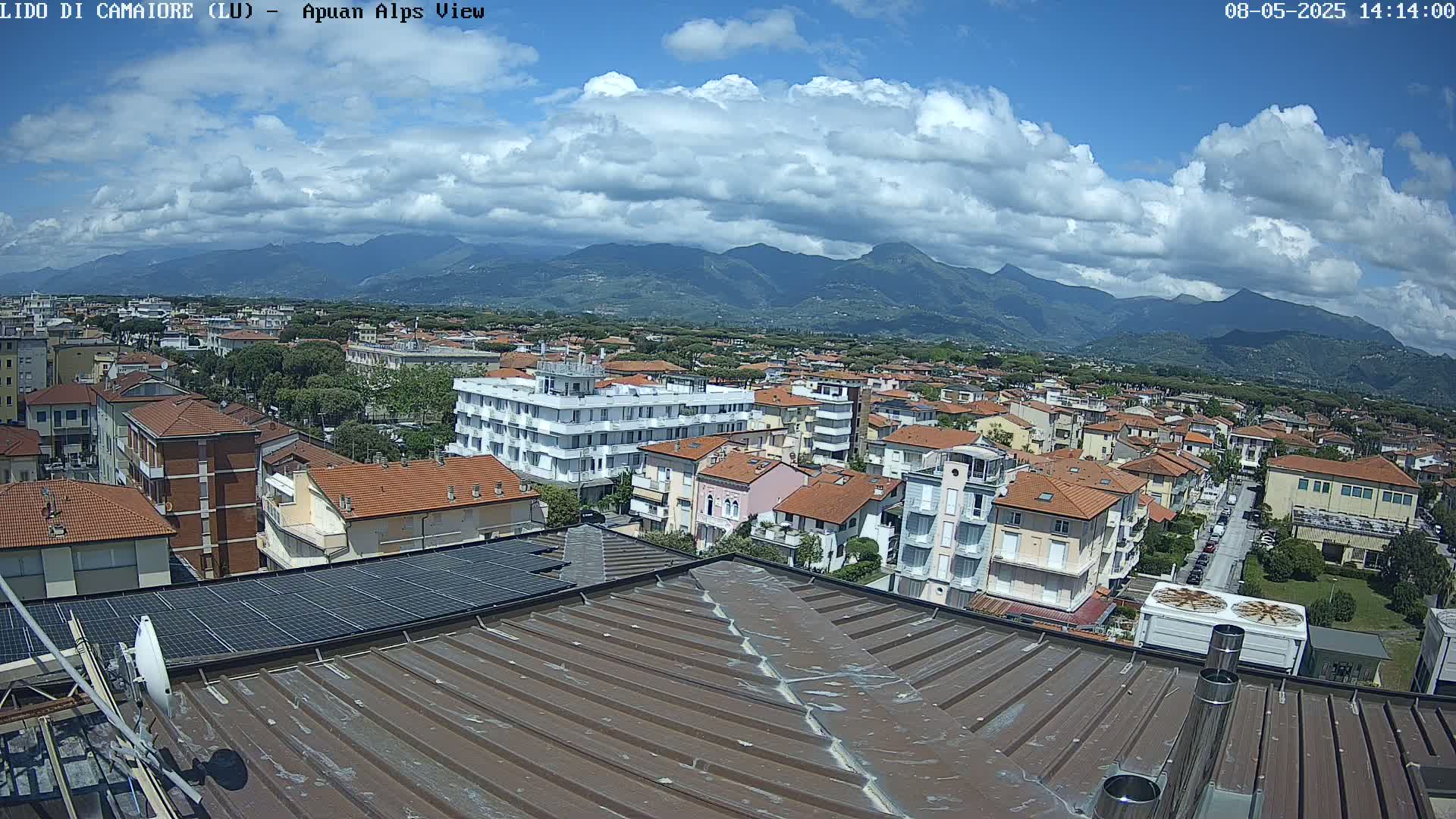 A partly cloudy day reveals a rooftop view of a town nestled against a mountain range.