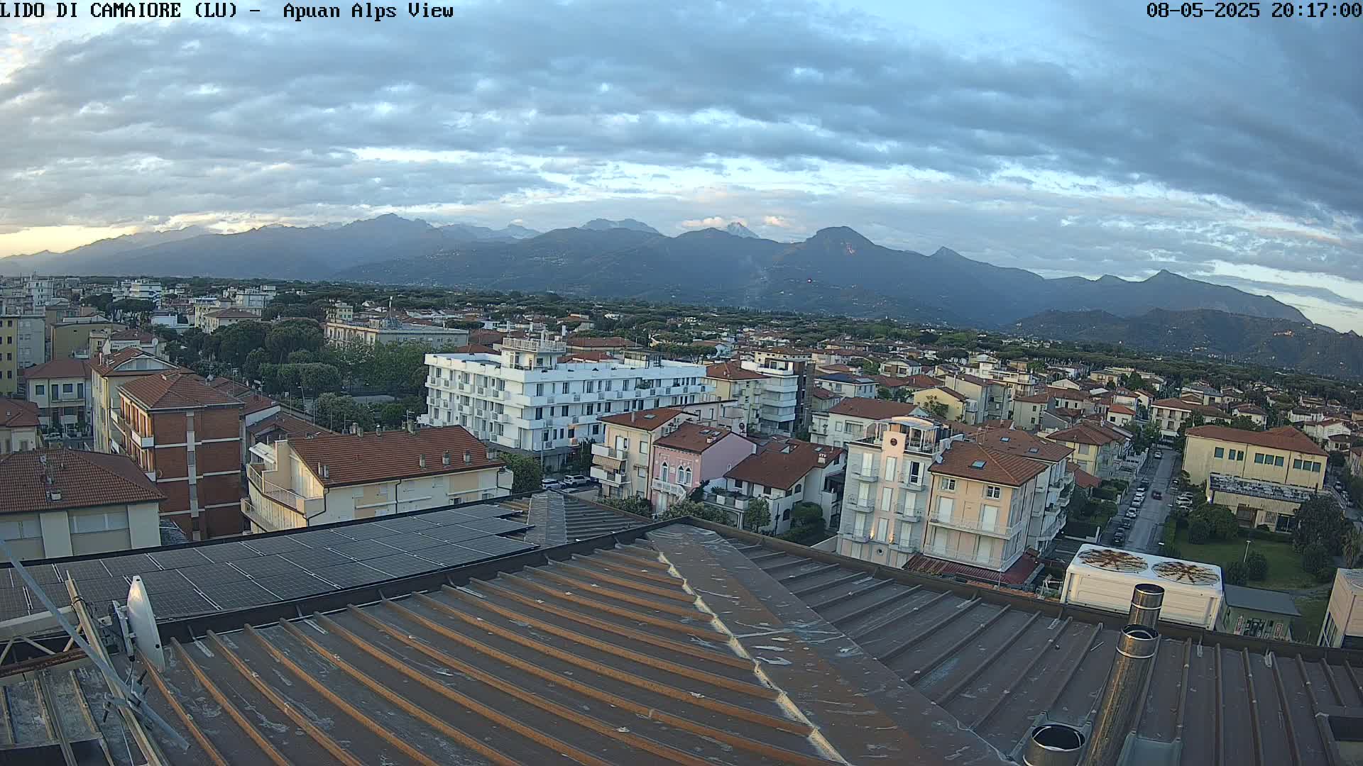 A rooftop view of a town nestled at the foot of mountains under a partly cloudy sky.