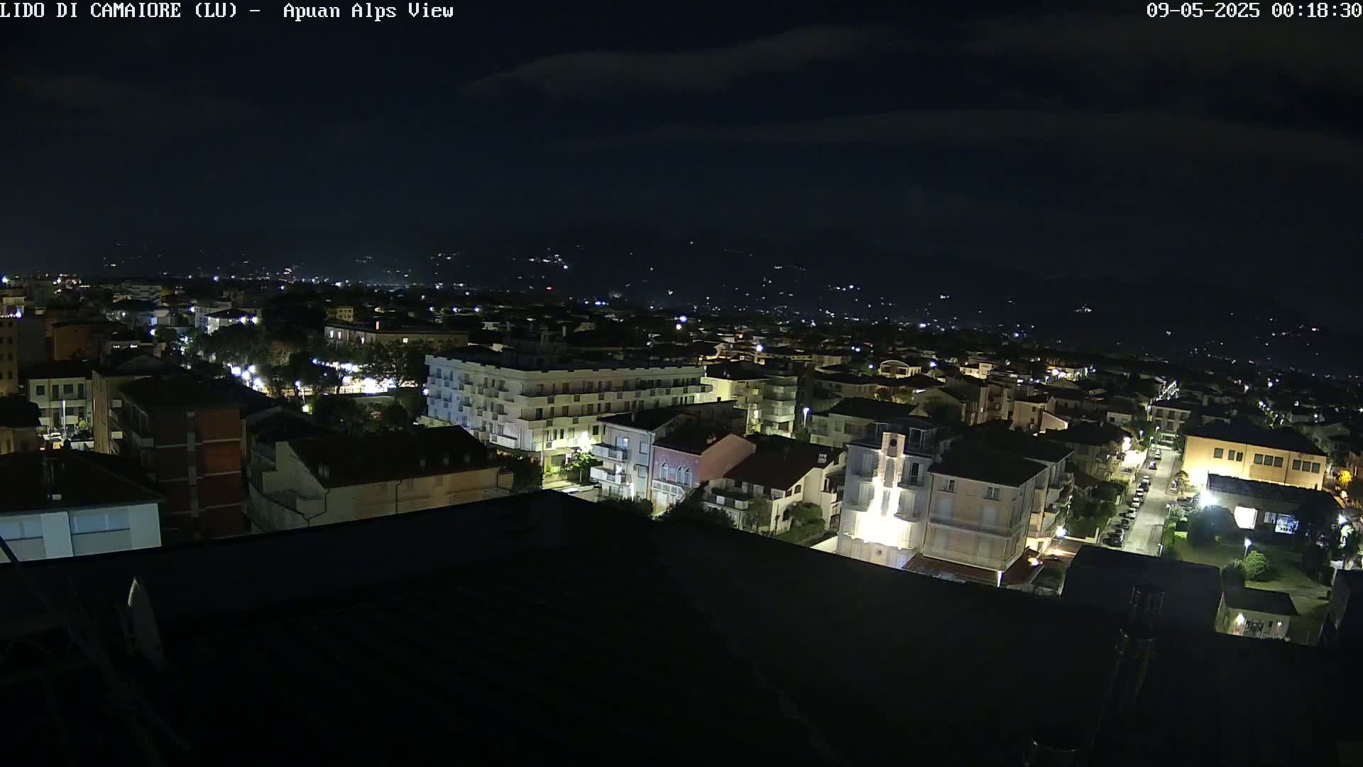 A nighttime, high-angle view of a town illuminated by streetlights, with a distant mountain range visible under a dark sky.
