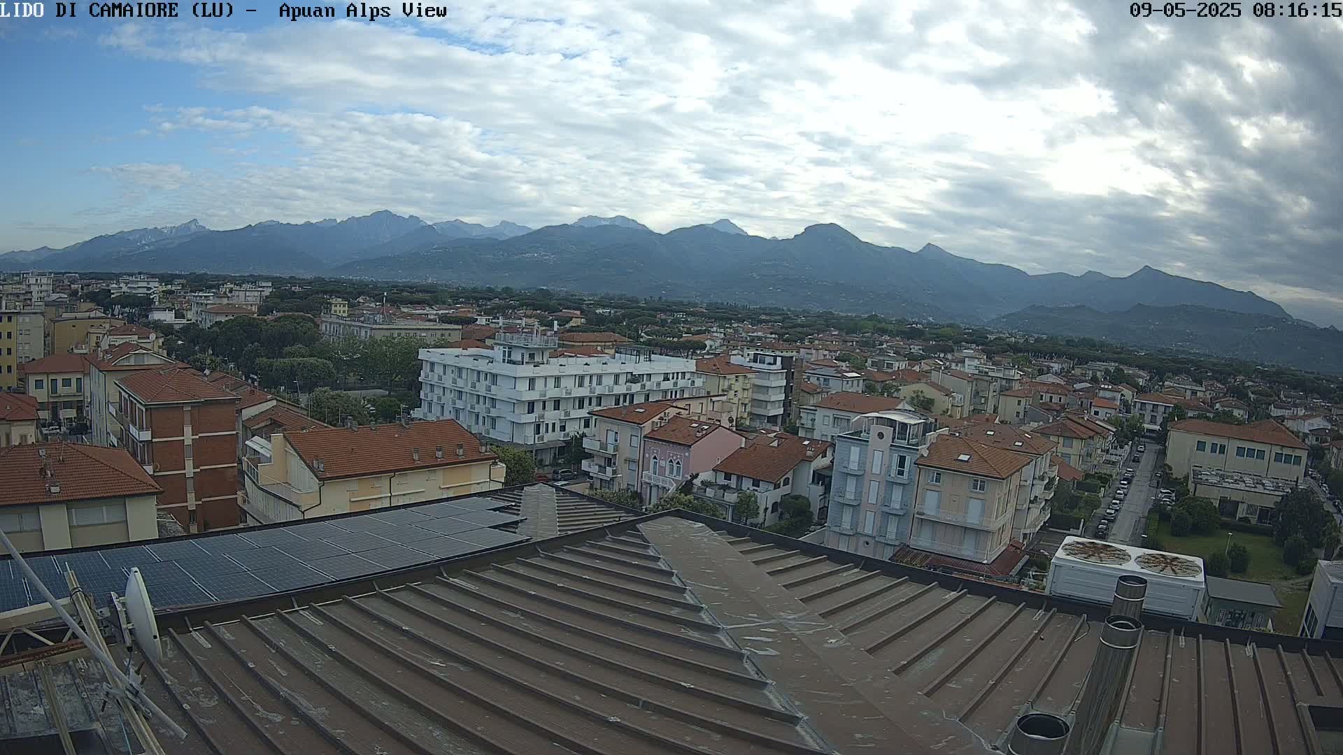 A rooftop view of a town nestled beneath a mountain range on an overcast day.