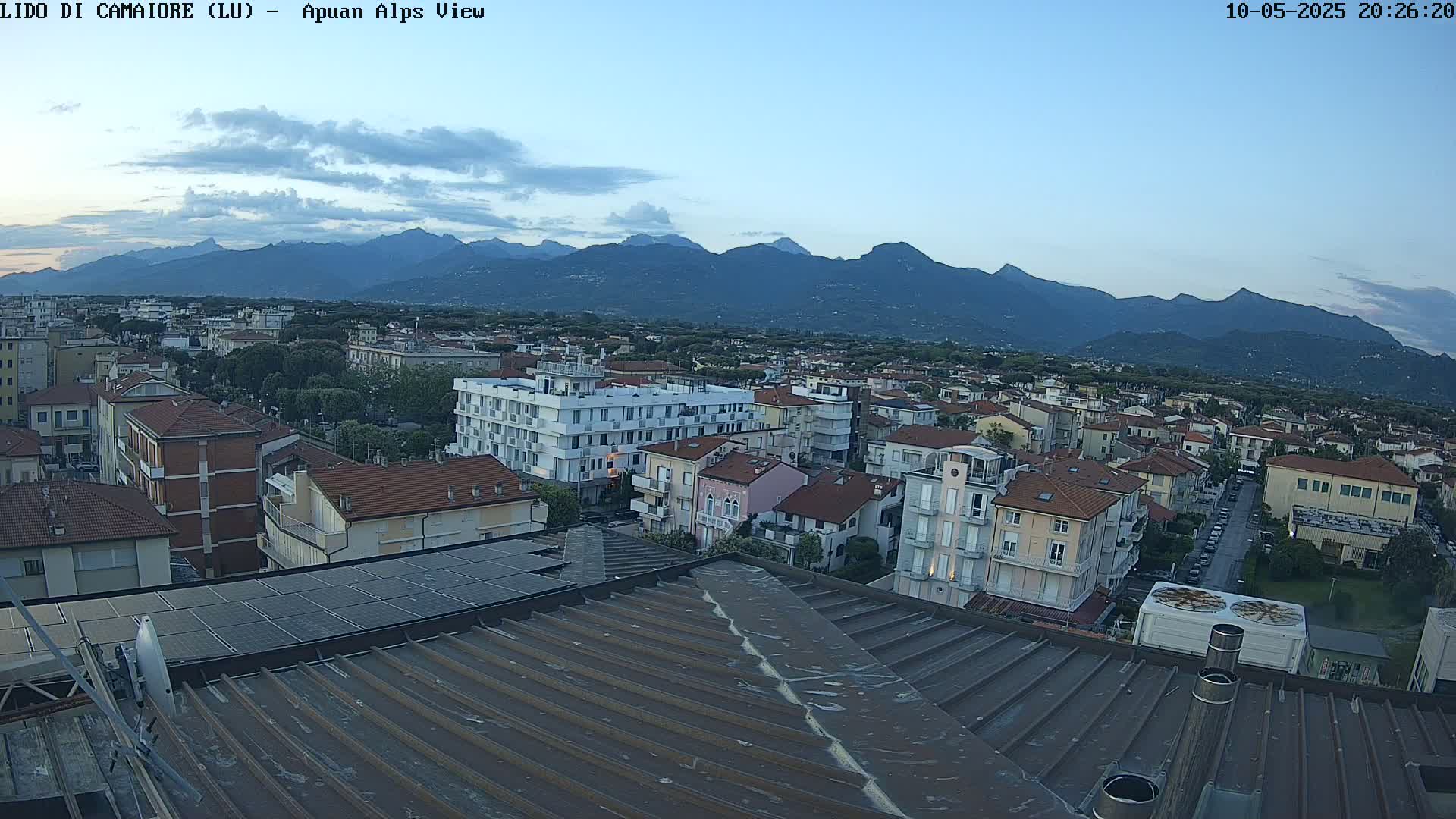 A rooftop view of a town at dusk, with a mountain range visible in the background under a mostly clear sky.
