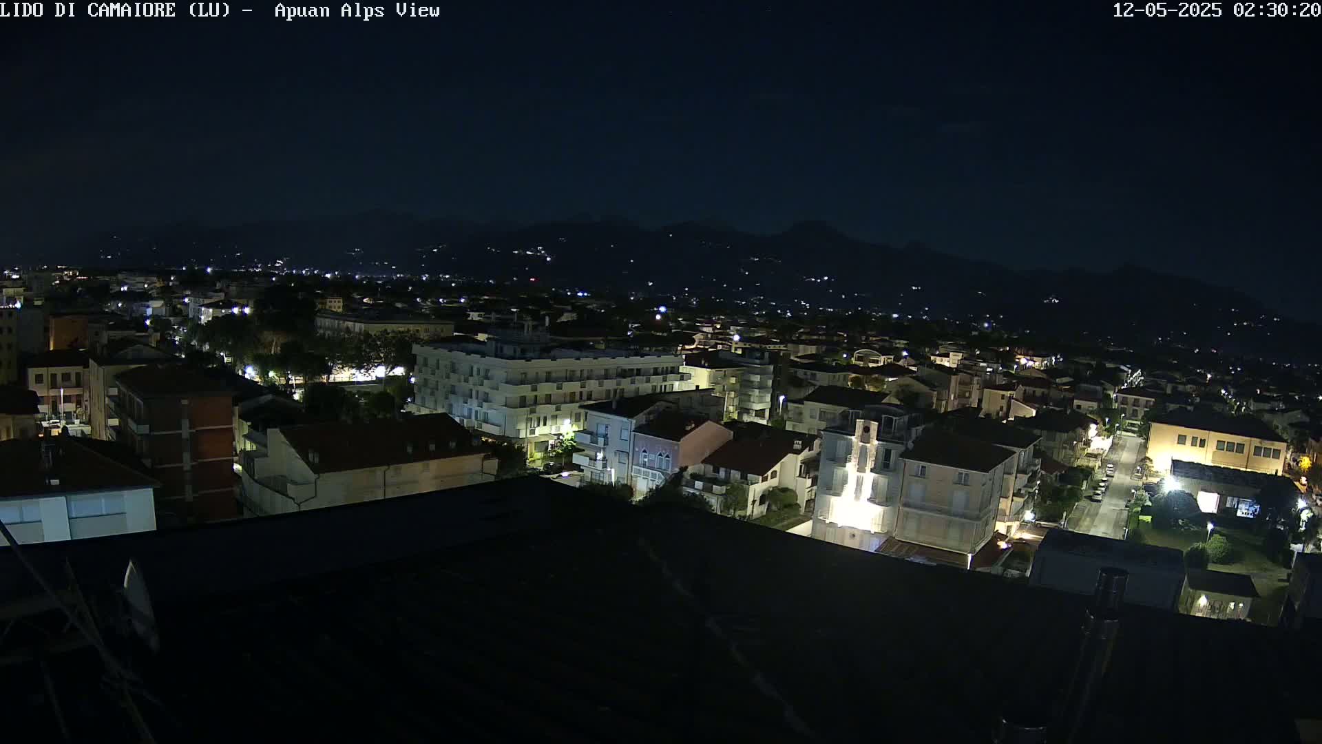 A nighttime aerial view of a town nestled against dark mountains under a clear, dark sky.