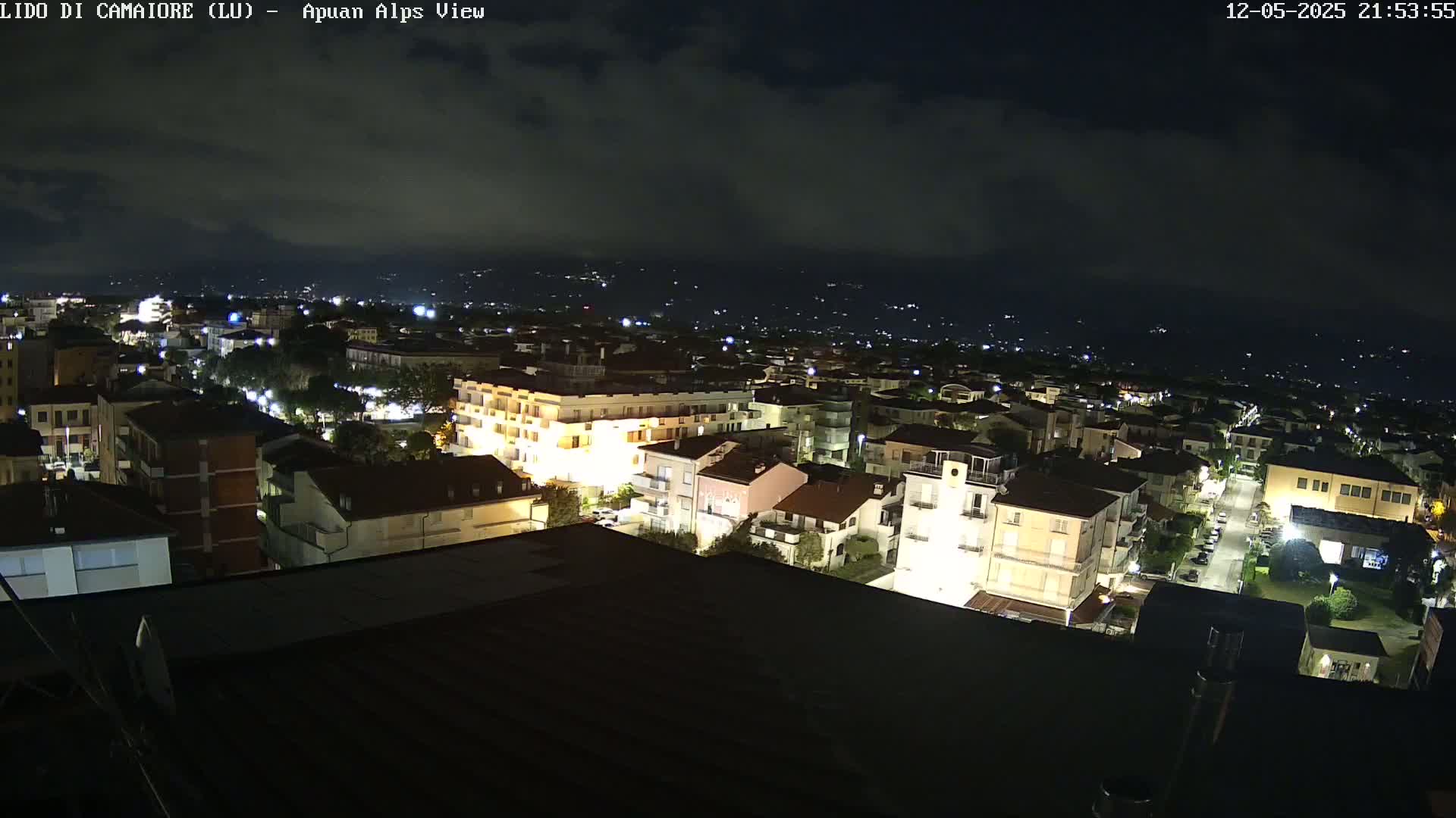 A nighttime, high-angle view of a town illuminated by streetlights and building lights under a cloudy sky.