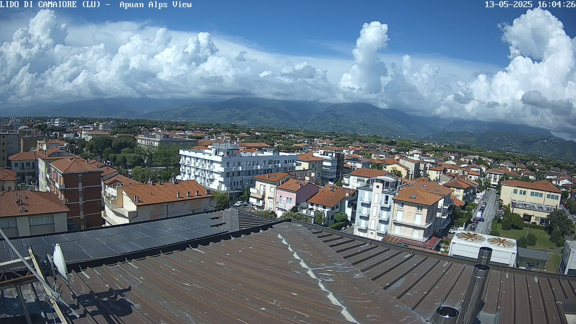 A partly cloudy sky overlooks a town of low-rise buildings, with mountains visible in the distance.