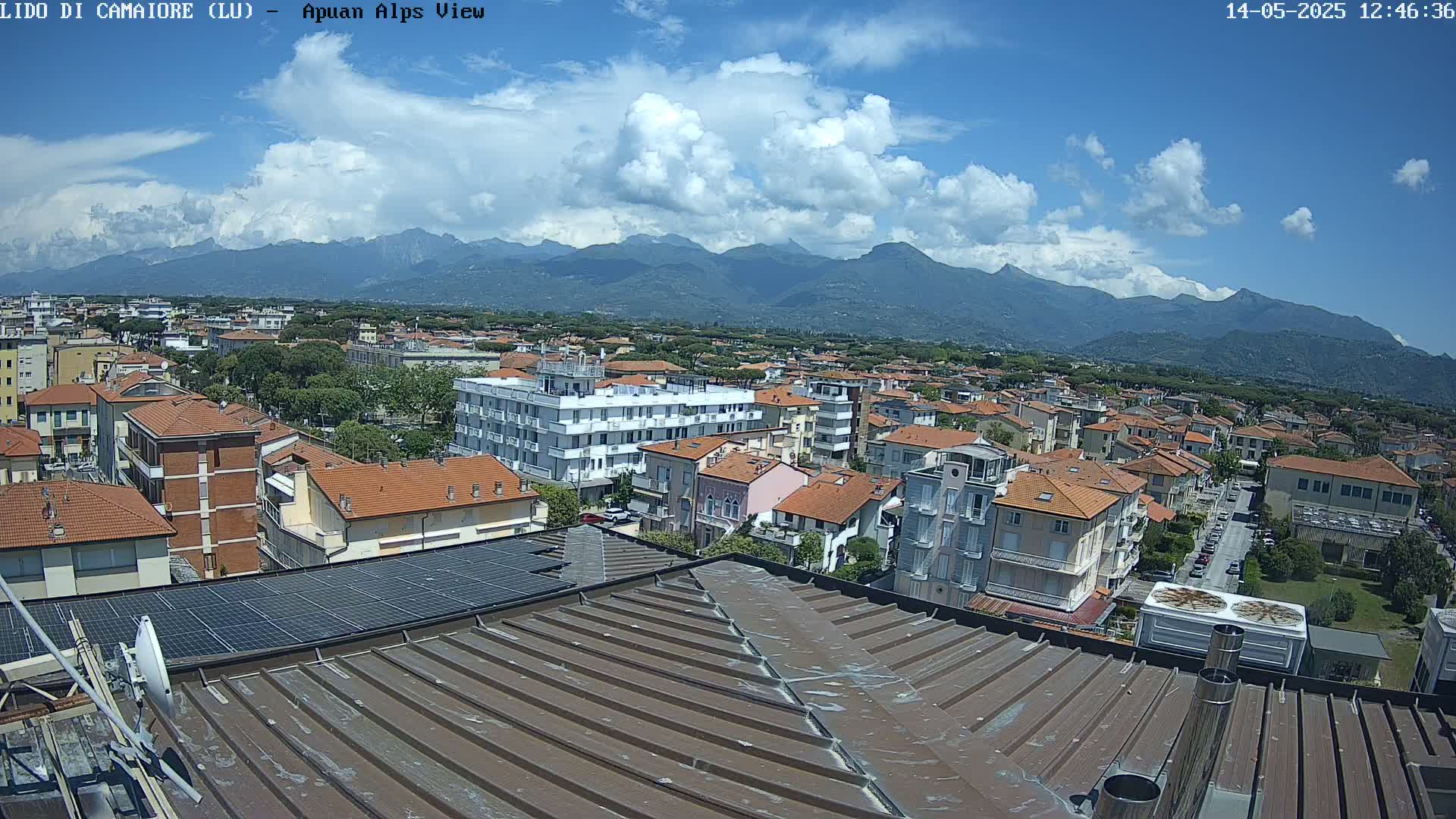A partly cloudy sky overlooks a town of low-rise buildings nestled against a mountain range.