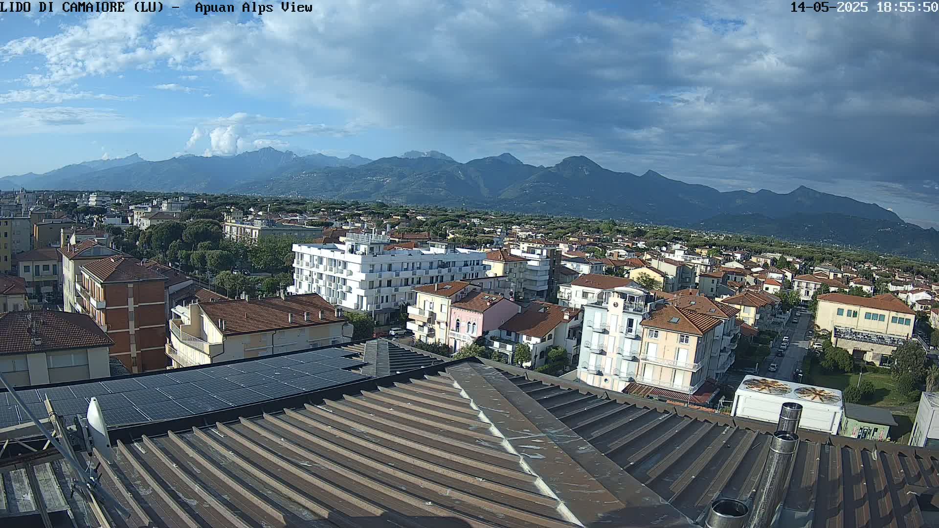 A partly cloudy sky overlooks a town of low-rise buildings with a mountain range in the background.