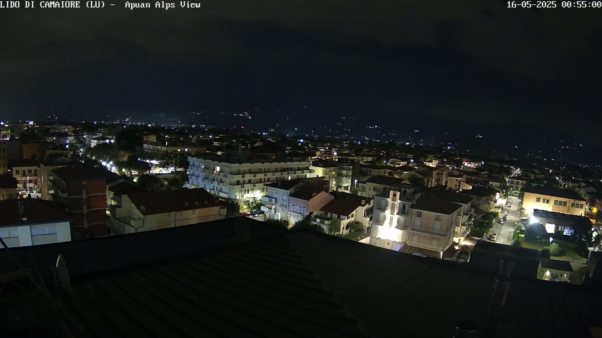 A nighttime aerial view of a town shows numerous buildings with some lights on, under a dark sky.