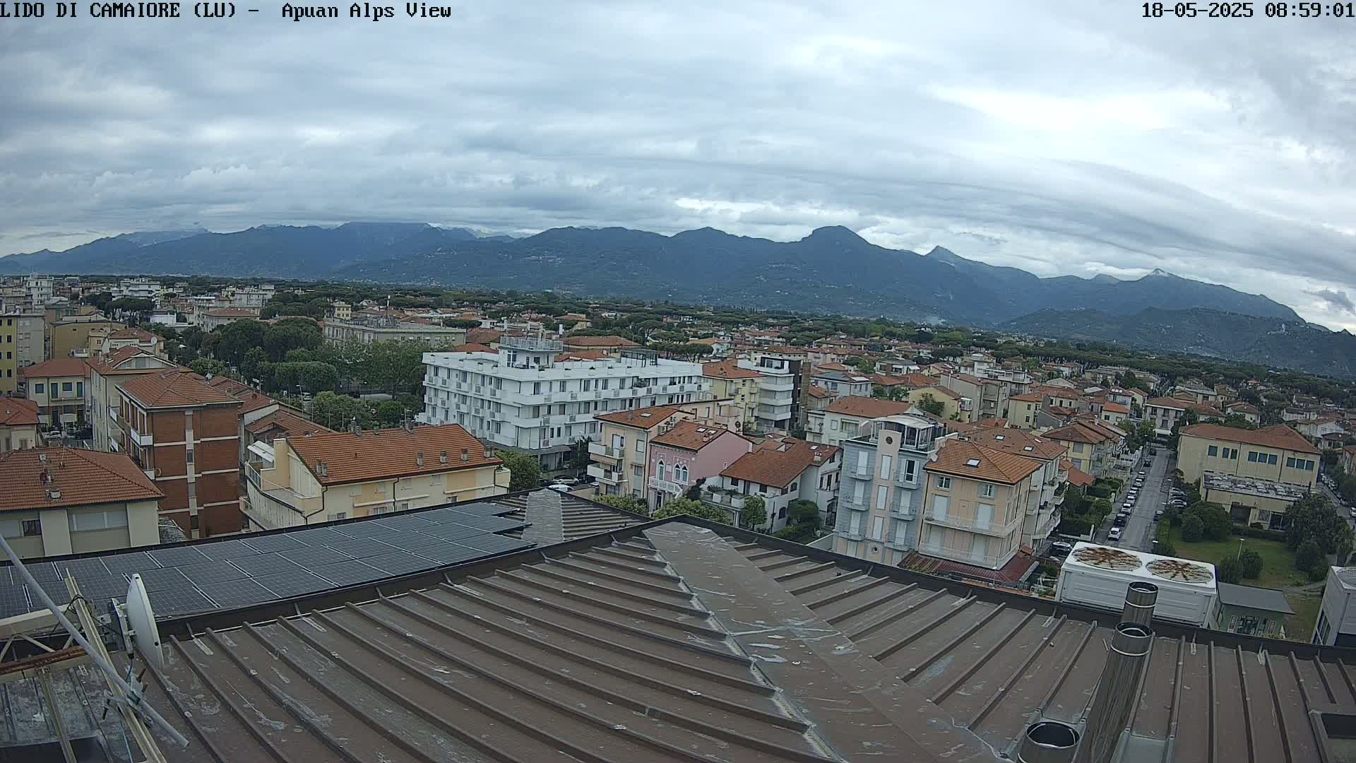 A rooftop view of a town under a cloudy sky, with mountains in the distance.