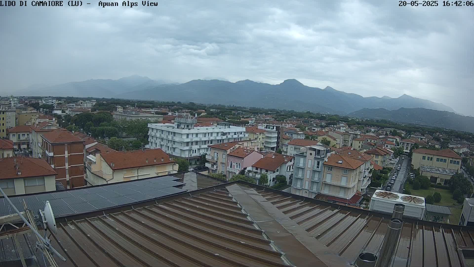A wet rooftop overlooks a town nestled against a mountain range under a cloudy sky.