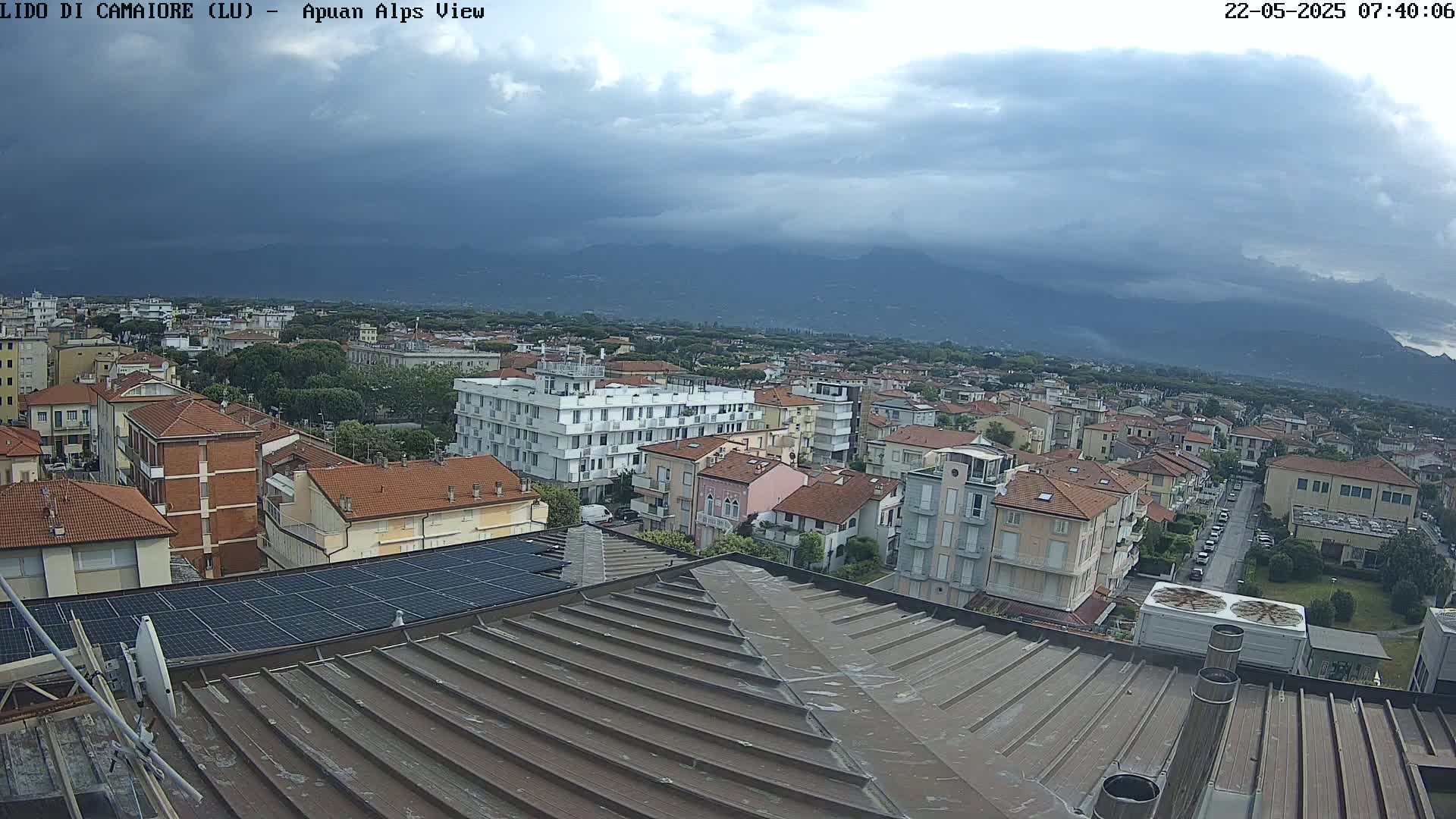 A rooftop view of a town under a cloudy sky, with mountains in the distance.