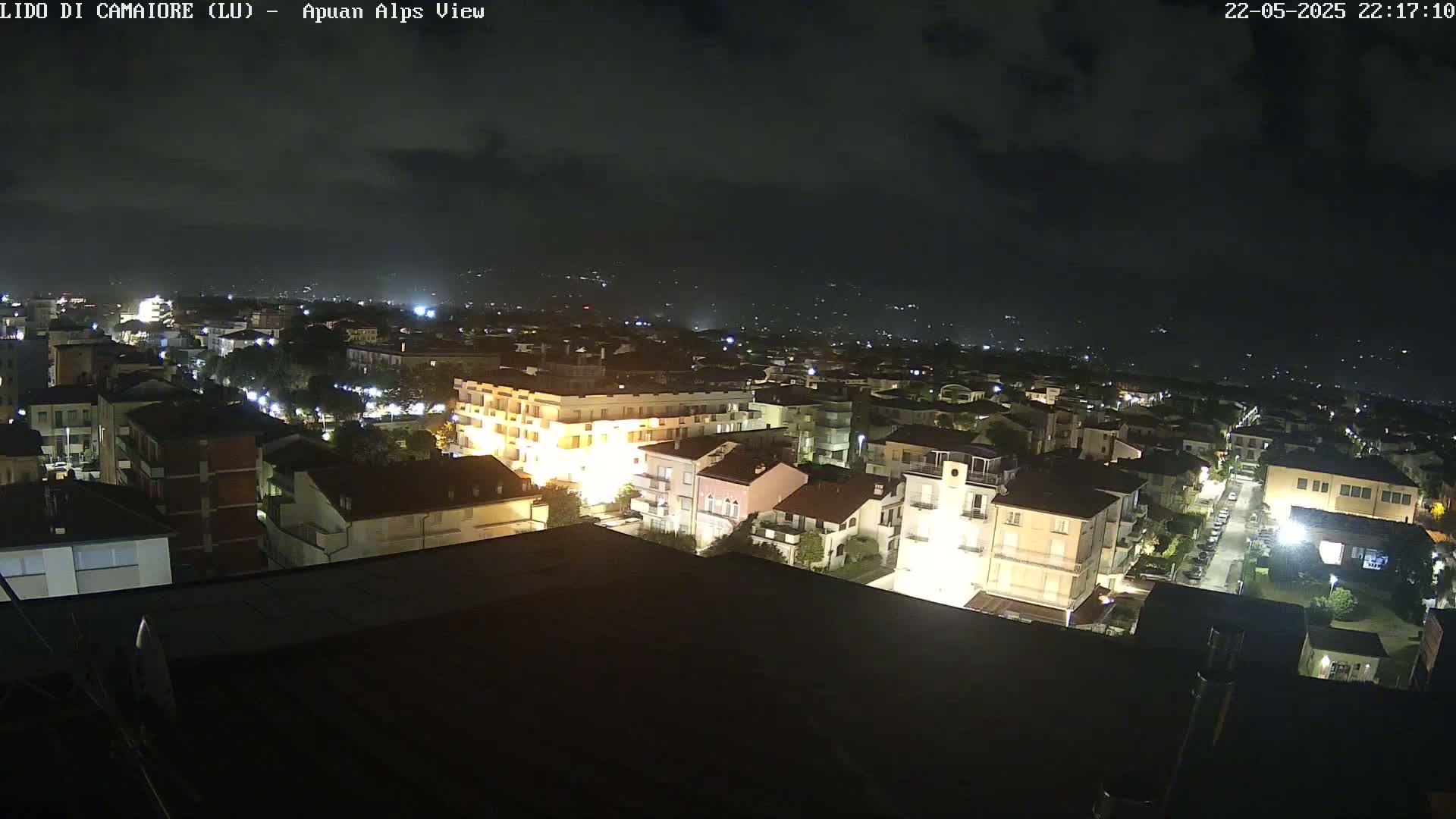 A nighttime, high-angle view of a town with buildings illuminated, under a partly cloudy sky.