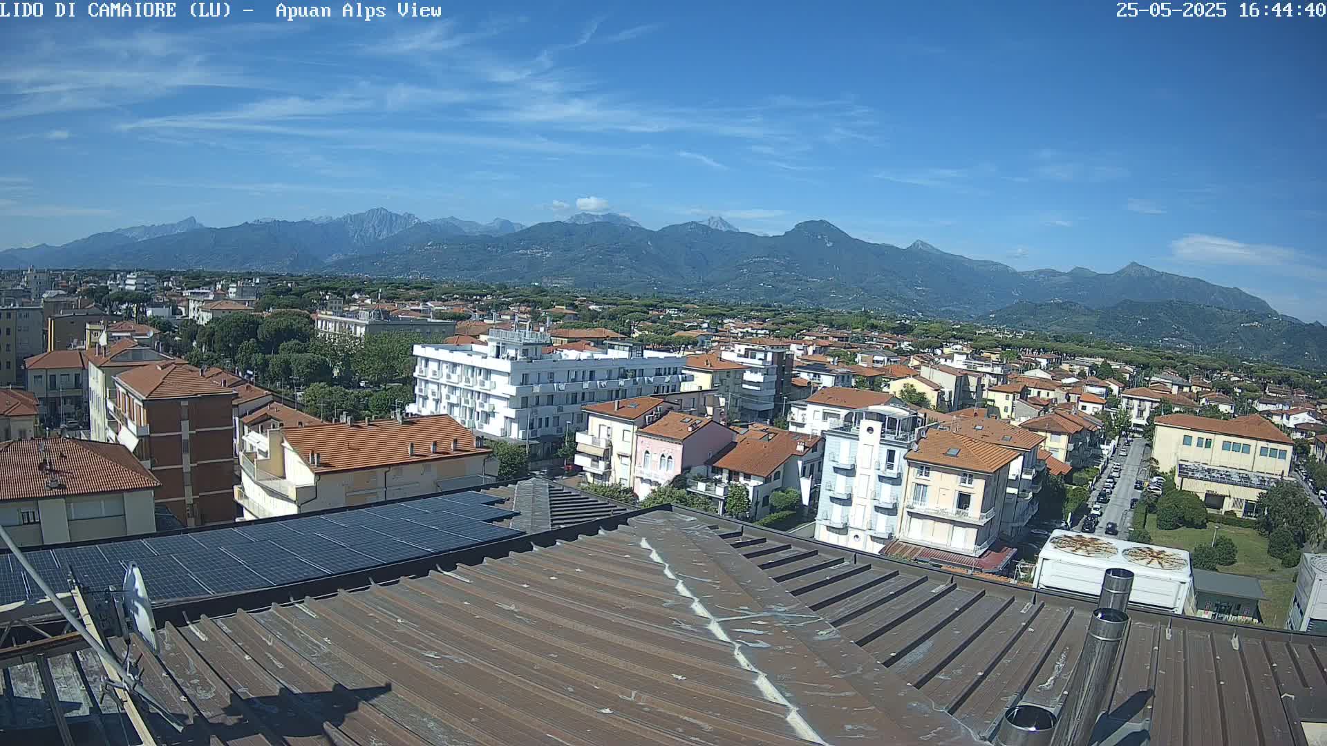A rooftop view of a town nestled against a mountain range under a clear, sunny sky.