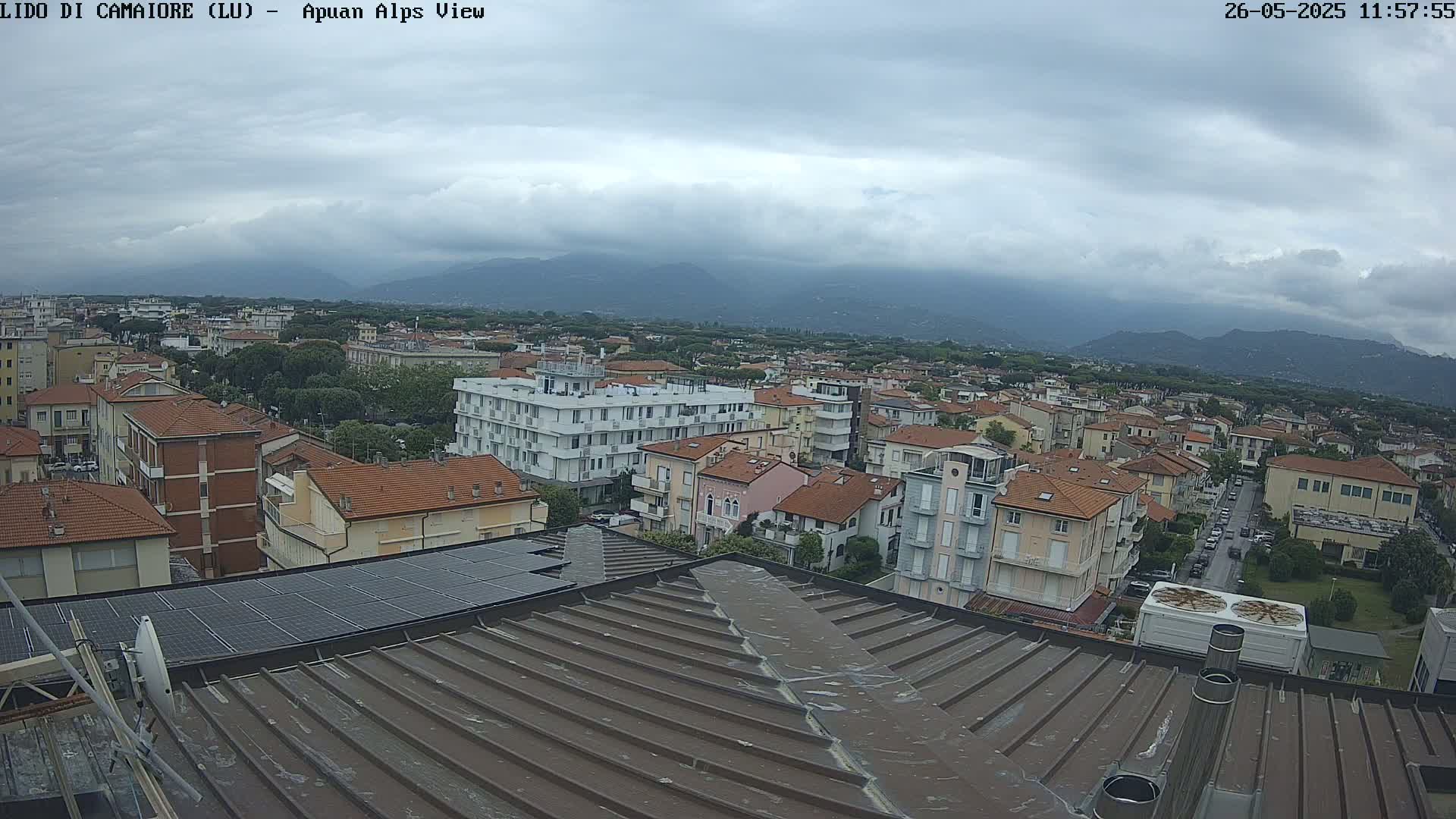 A rooftop view of a town under a cloudy sky, with mountains visible in the distance.