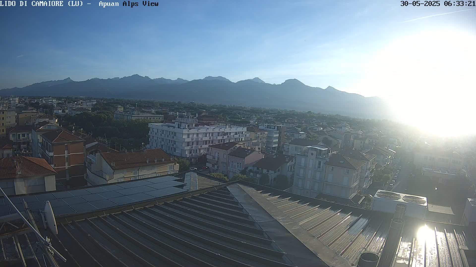A sunny morning view from a rooftop overlooking a town nestled against a mountain range.