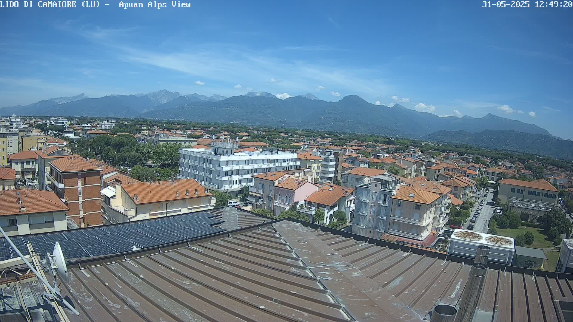 A rooftop view of a town nestled against a mountain range under a mostly clear blue sky.