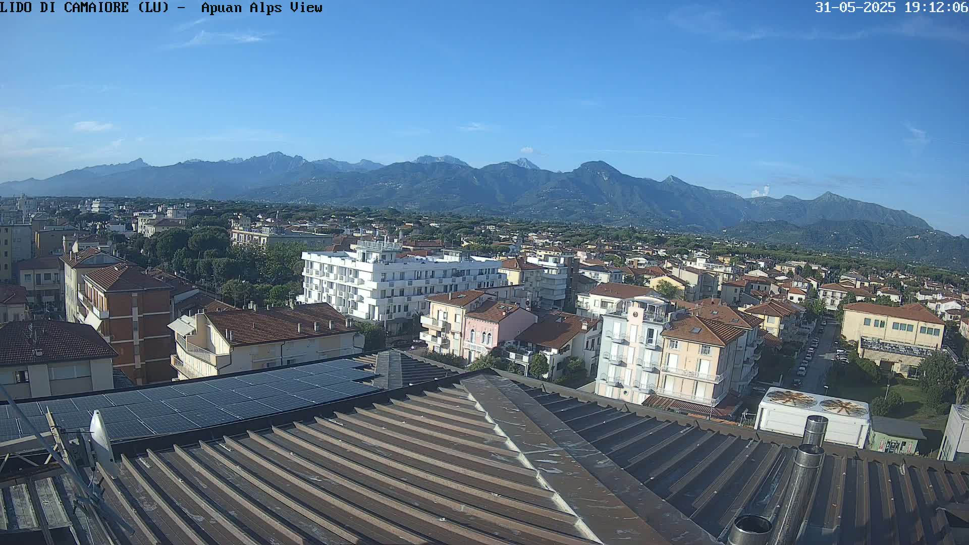 A rooftop view overlooking a town nestled beneath a mountain range on a clear, sunny day.