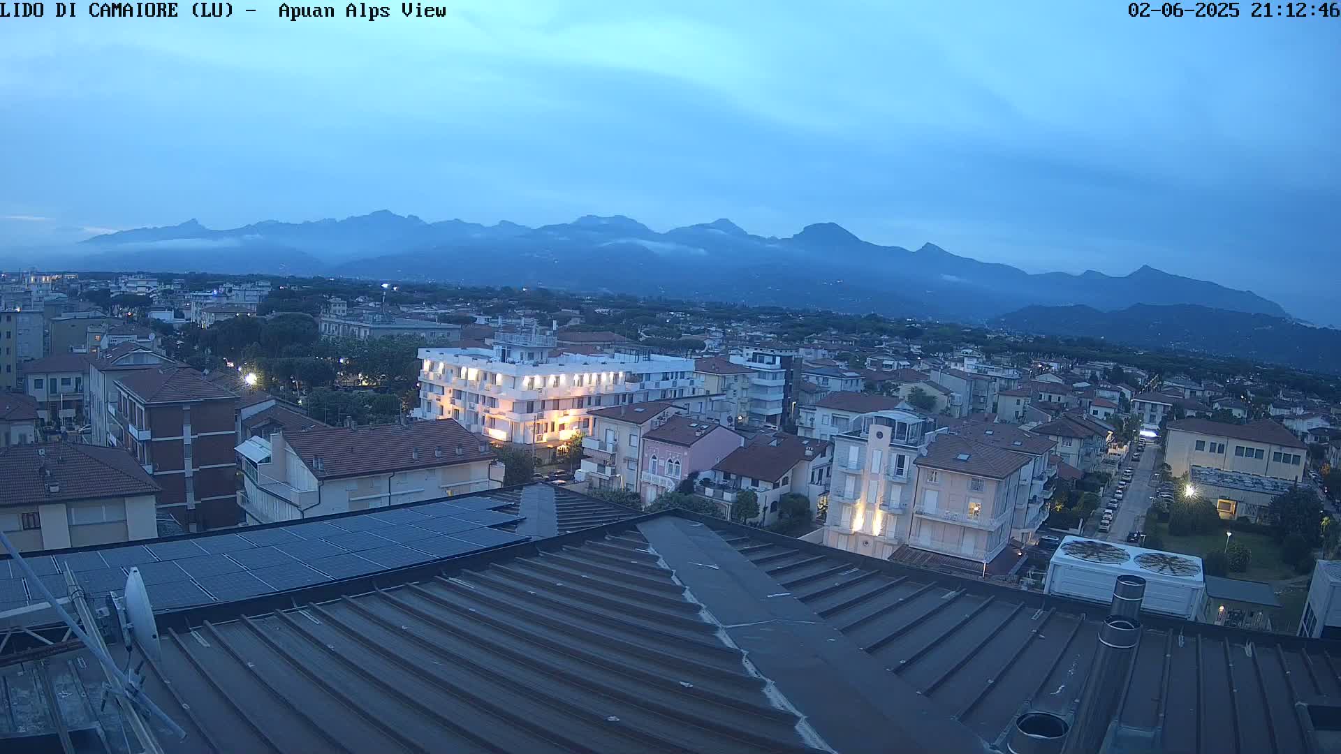 An aerial evening view of a town nestled at the base of a mountain range under a twilight sky.