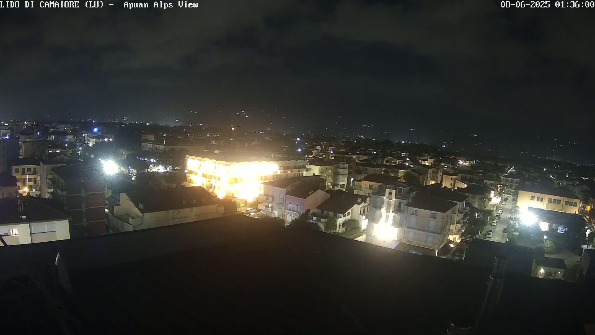 A nighttime, aerial view of a town illuminated by streetlights and building lights under a mostly clear sky.