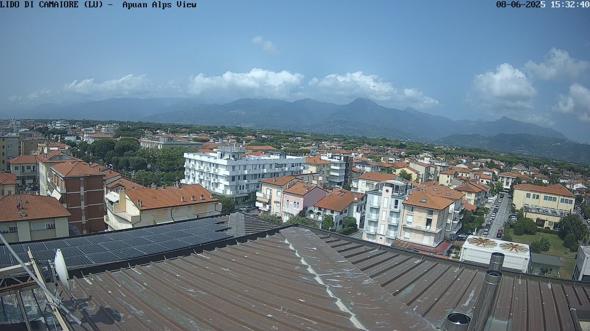 A rooftop view of a town nestled against a mountain range under a partly cloudy sky.