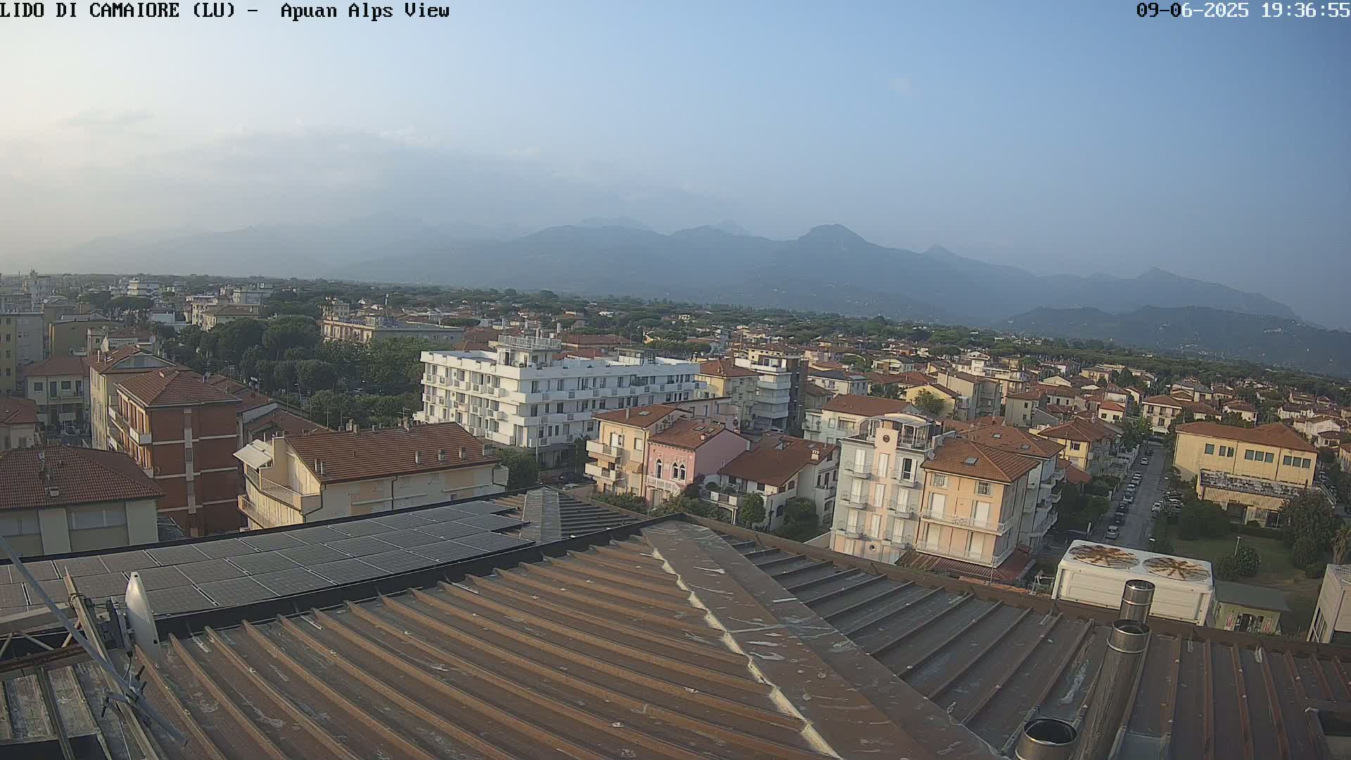 A rooftop view of a town, under a clear sky, with mountains visible in the distance.