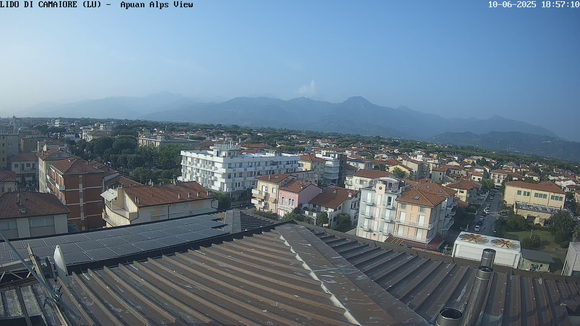 A rooftop view of a town shows a clear, sunny day with distant mountains in the background.