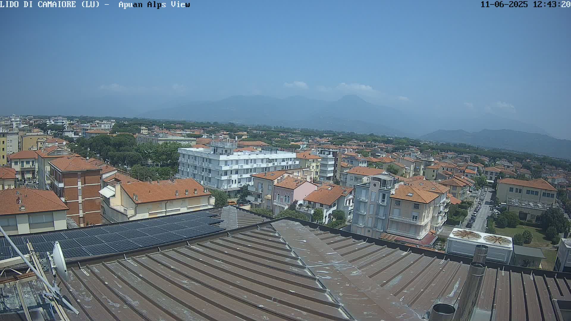 A clear, sunny day shows a view of a town with many low-rise buildings, extending to distant mountains.