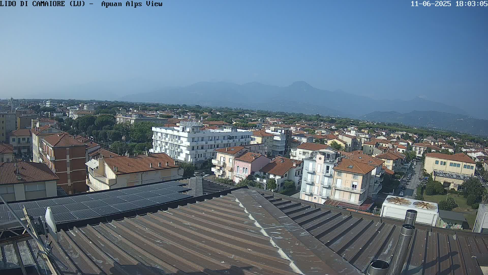 A rooftop view of a town under a clear blue sky, with mountains visible in the distance.