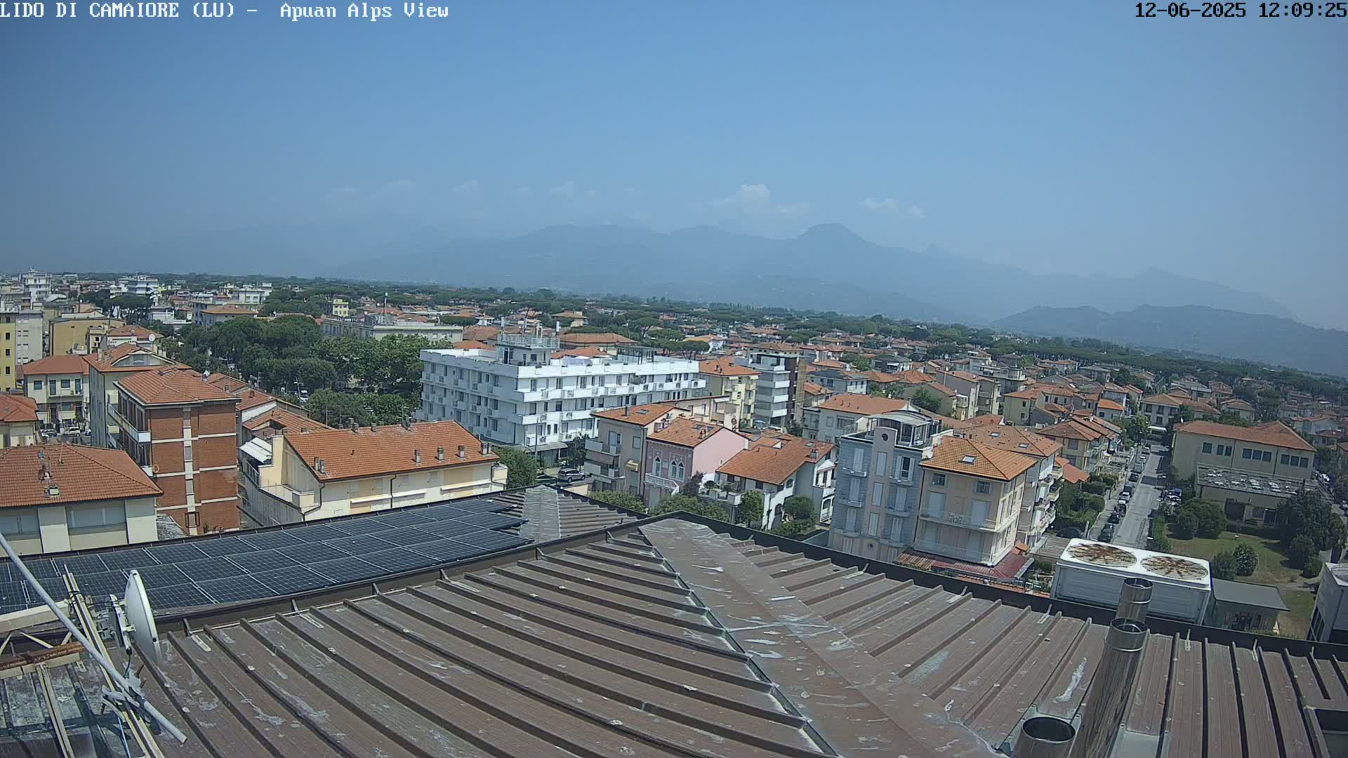 A rooftop view of a town under a clear blue sky, with mountains visible in the distance.