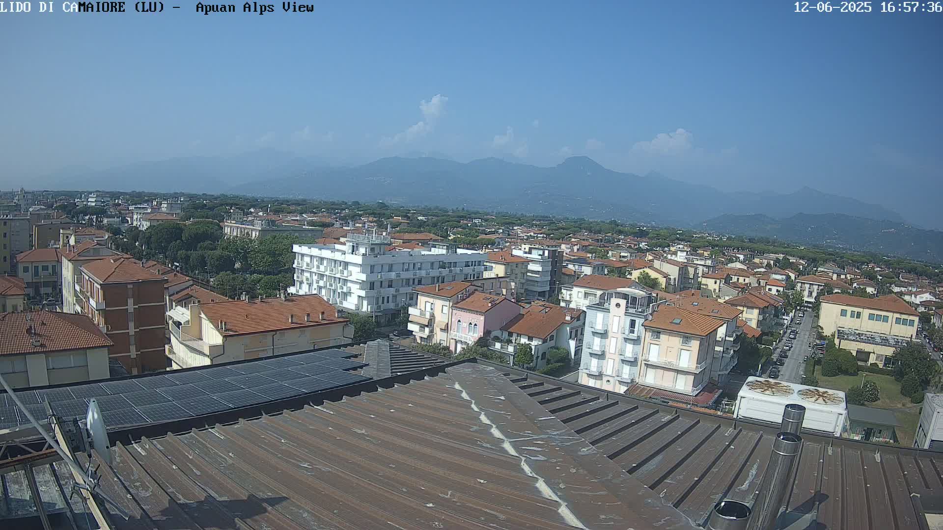 A rooftop view of a town under a mostly clear blue sky, with distant mountains visible in the background.