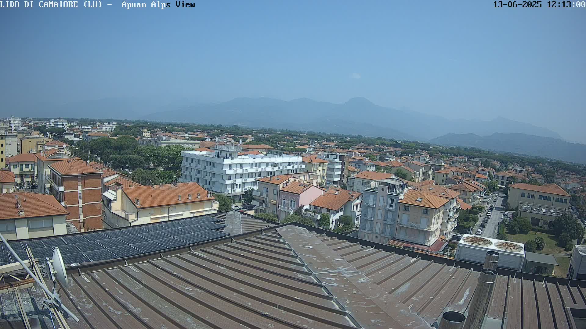 A rooftop view of a town under a clear blue sky, with mountains visible in the distance.