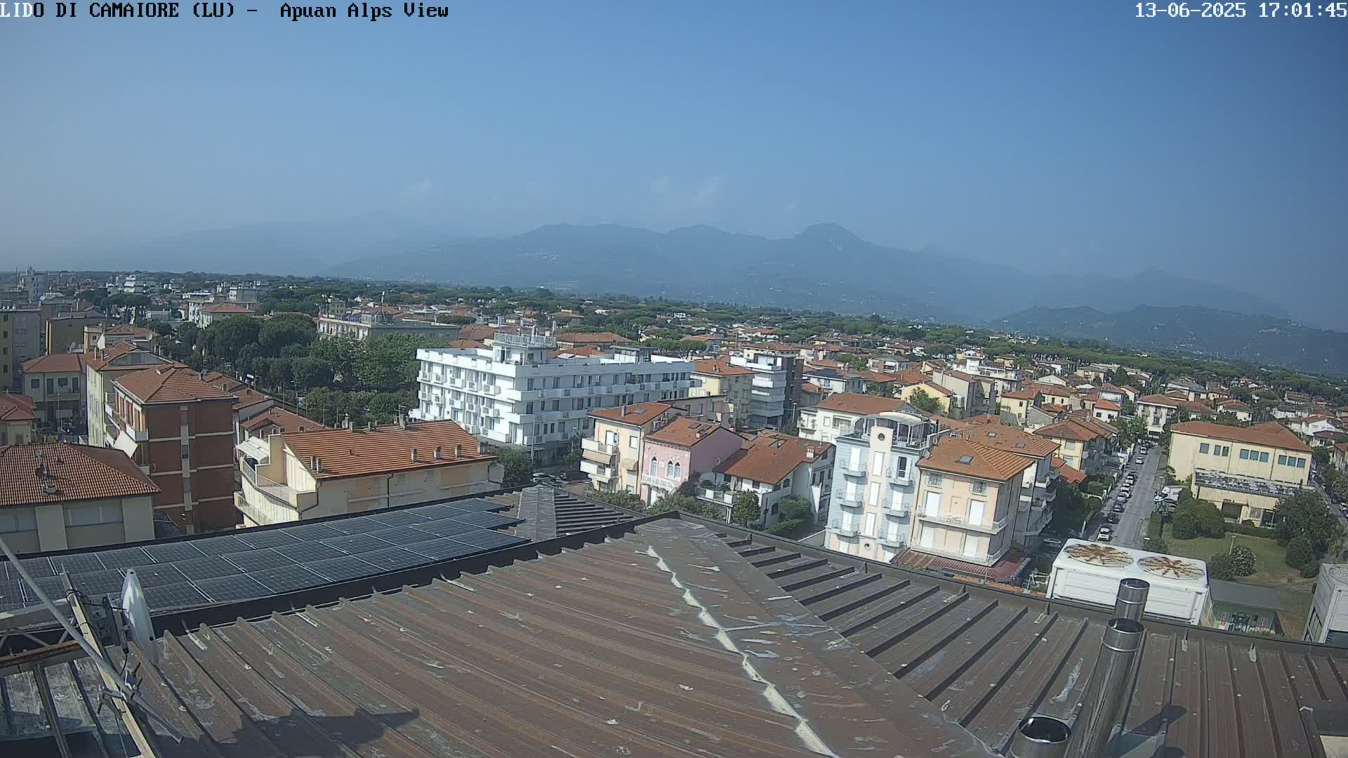 A rooftop view of a town under a clear blue sky, with distant mountains visible in the background.