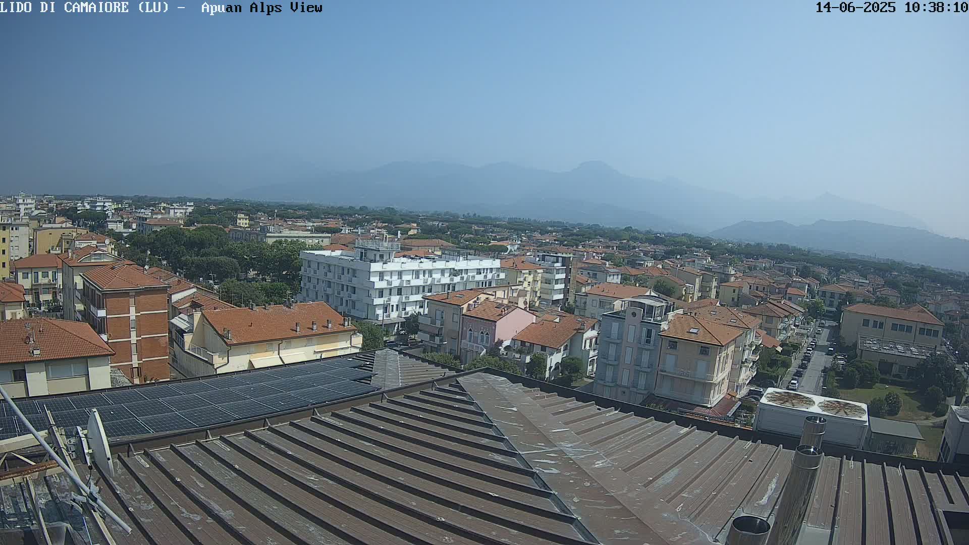 A rooftop view of a town on a clear, sunny day, with distant mountains visible in the background.