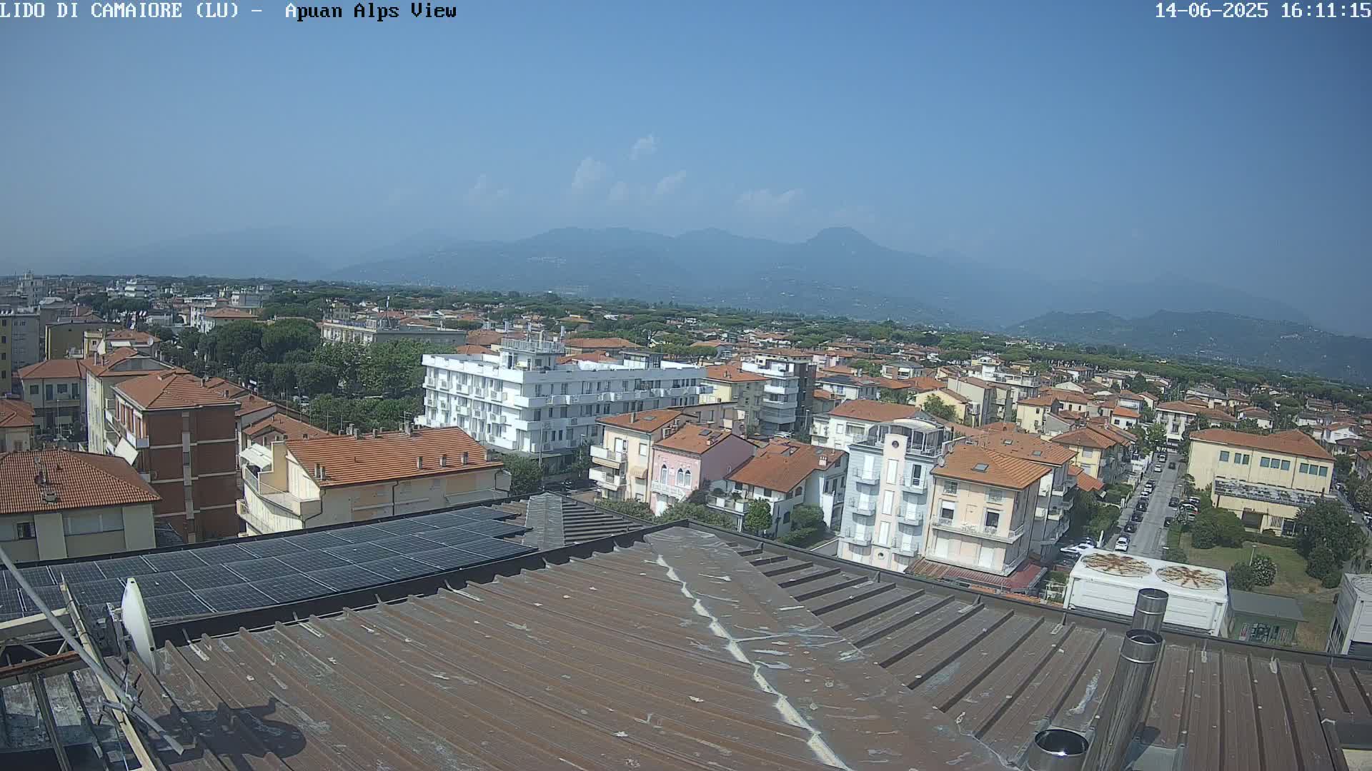 A rooftop view of a town on a clear, sunny day, with distant mountains visible in the background.