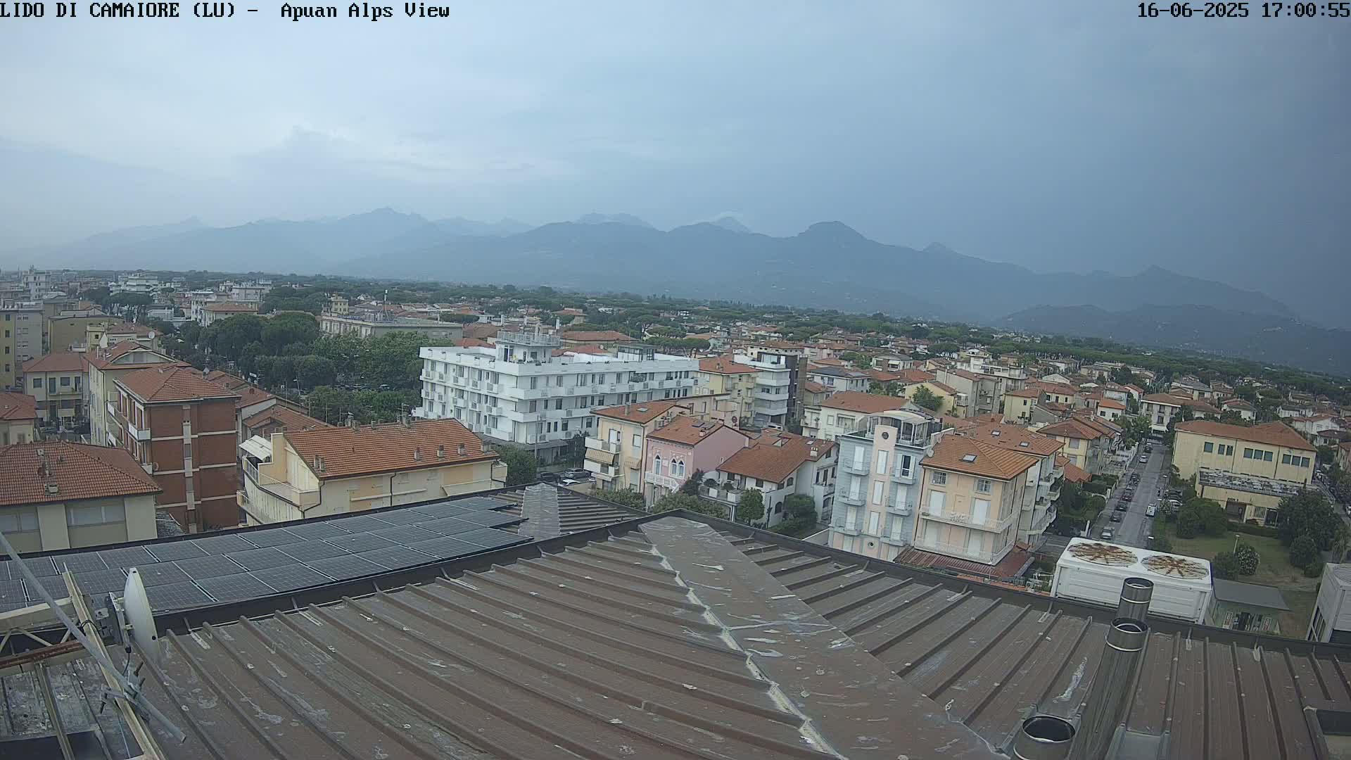 A rooftop view of a town under an overcast sky, with distant mountains visible in the background.
