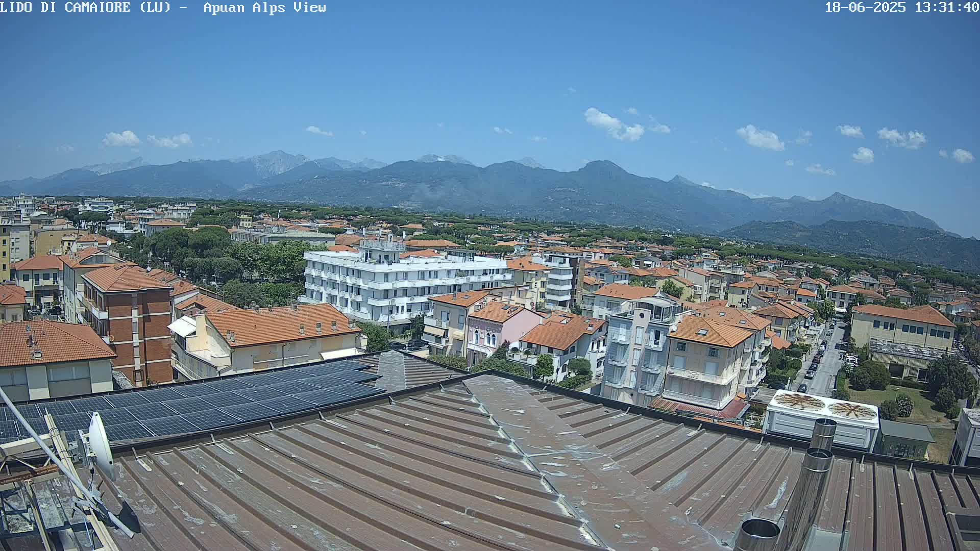 A rooftop view shows a town under a clear, sunny sky with mountains in the distance.