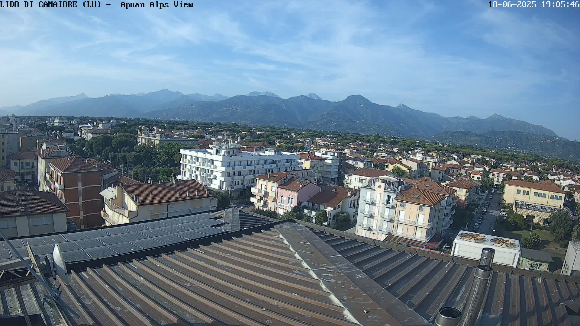 A clear day reveals a cityscape nestled beneath a mountain range, viewed from a rooftop with solar panels.