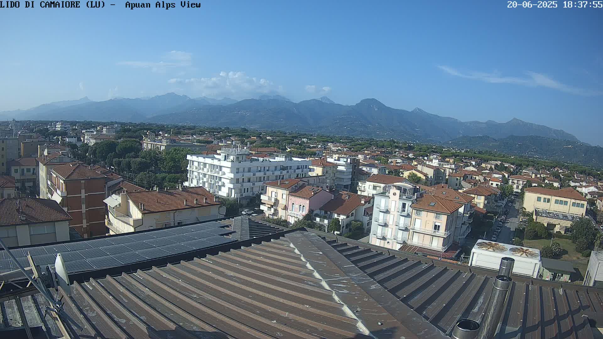 A rooftop view shows a town nestled beneath a clear blue sky and a mountain range in the distance.