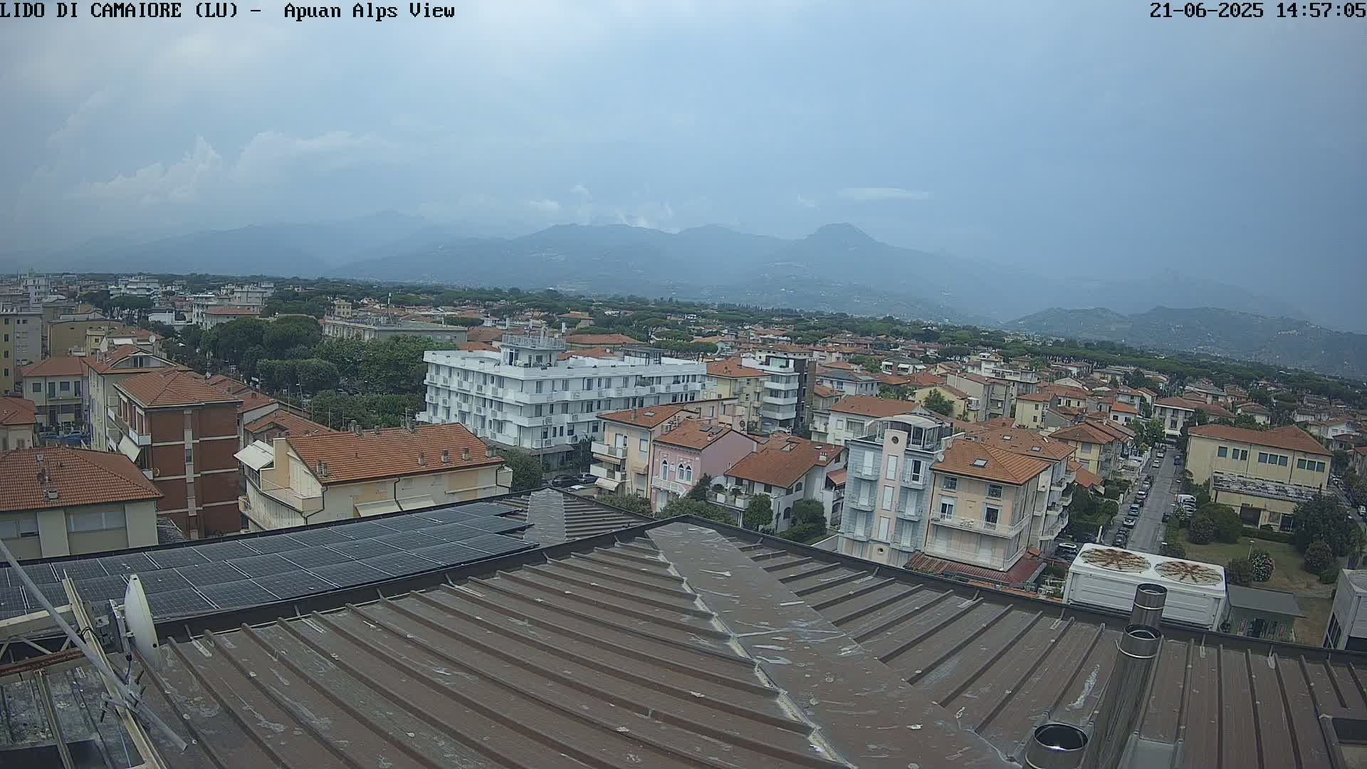 A rooftop view shows a town under an overcast sky with mountains in the distance.