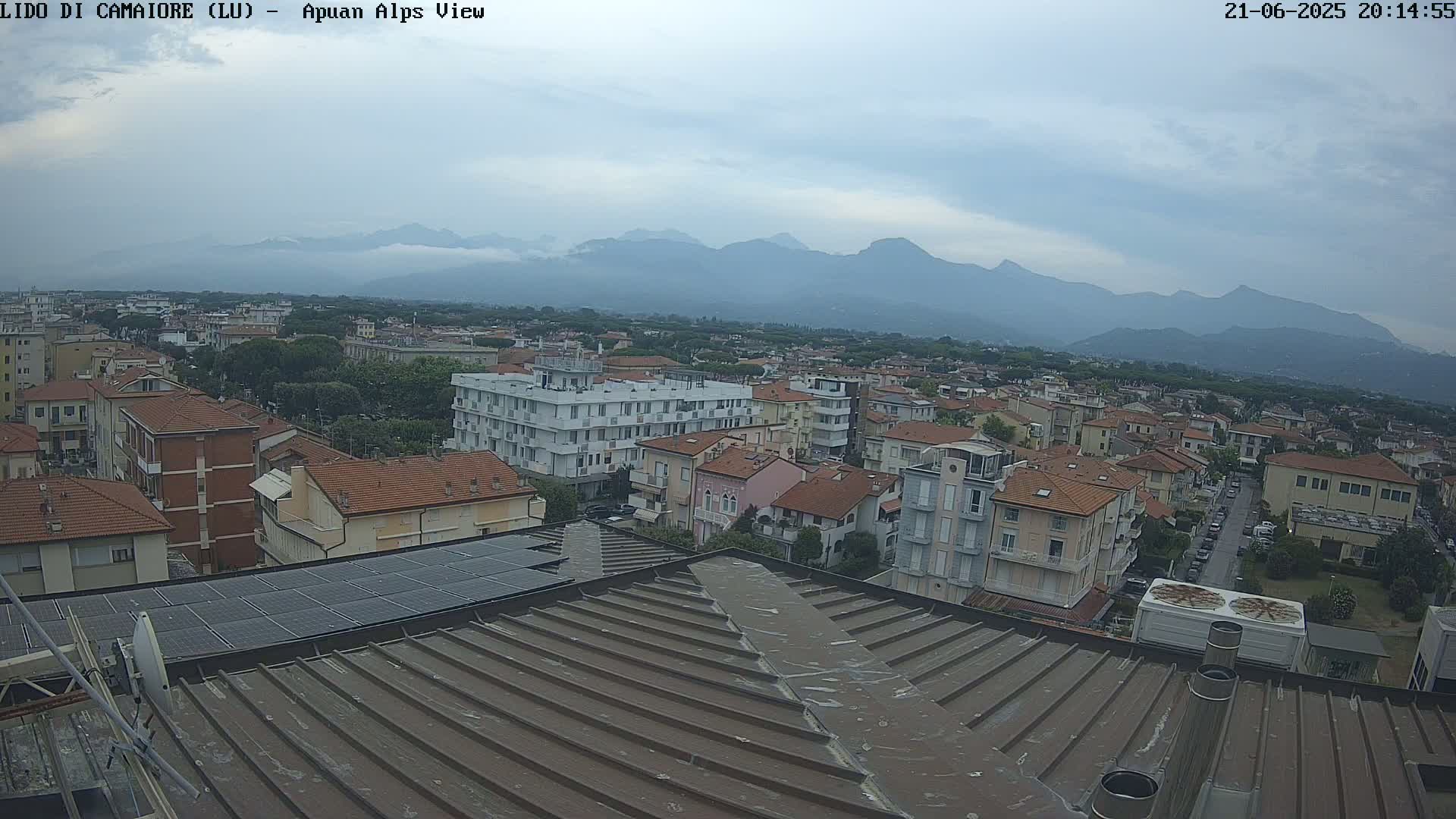 A view of a town with many low-rise buildings under an overcast sky, with mountains visible in the distance.